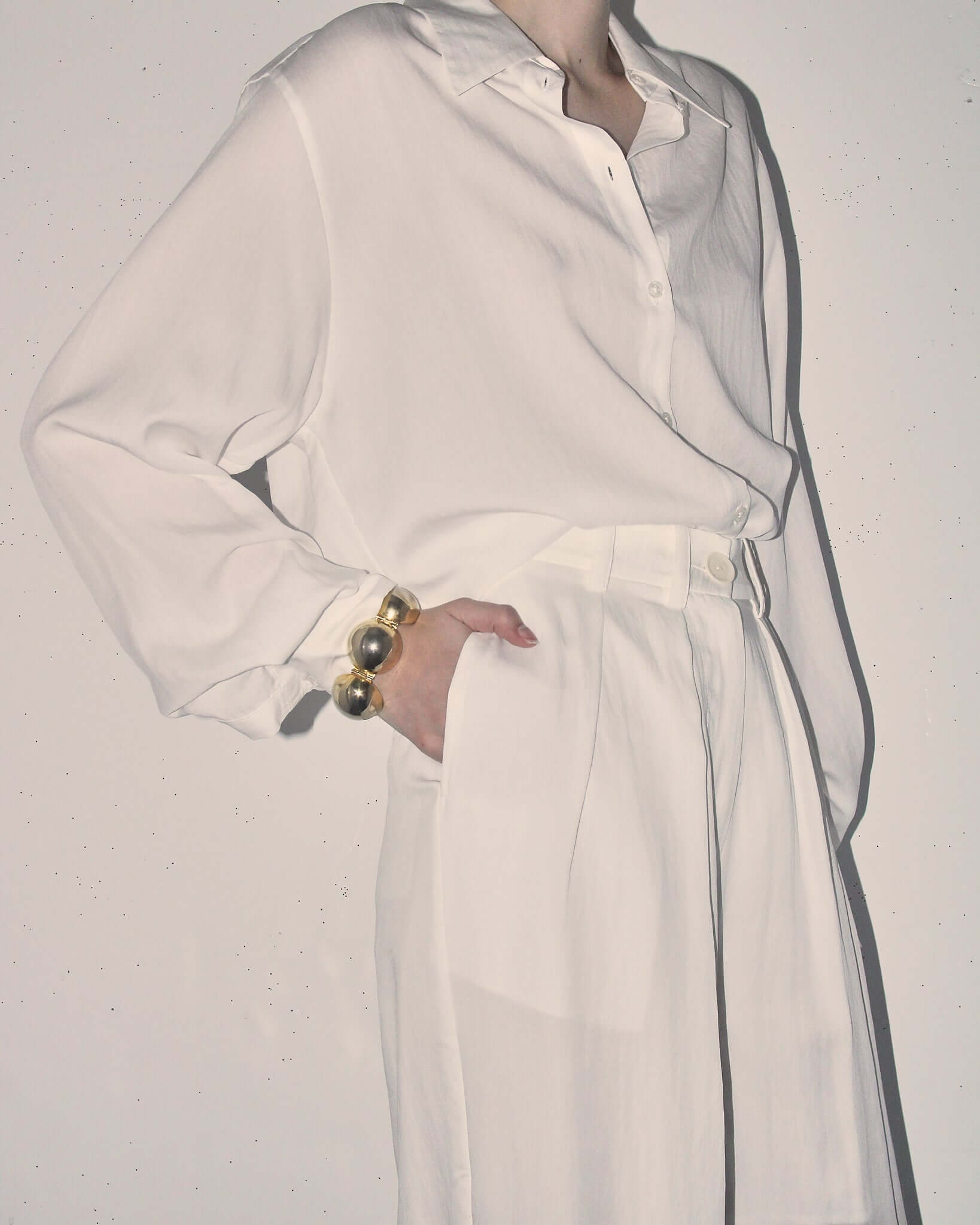 Detail shot of model wearing the 'Orla' Long Sleeve Shirt tucked into the matching 'Orla' pleated trousers as a set. with one hand in the pocket.