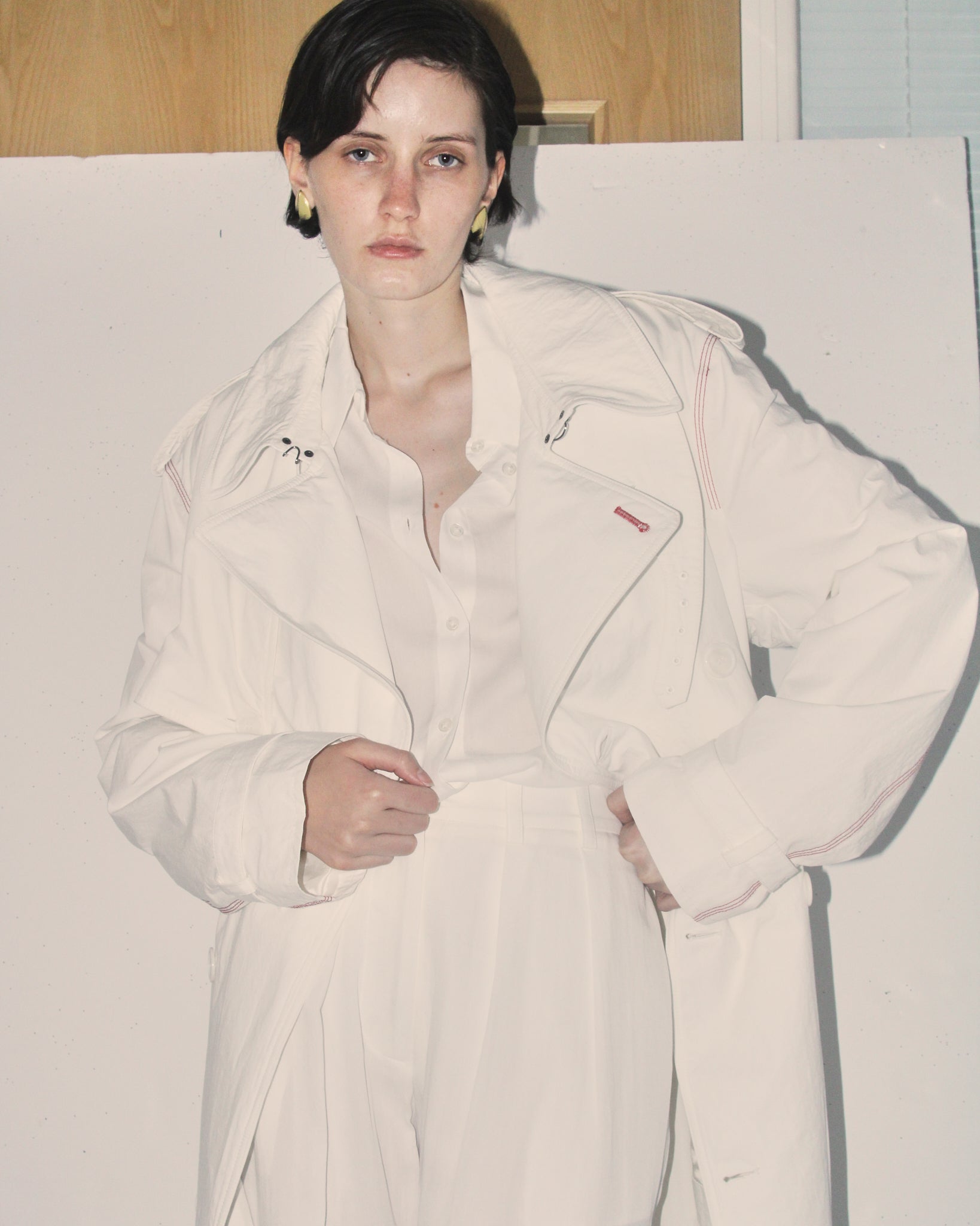 A detail shot of a model wearing the white 'Sophia' trench open, wearing a matching set of a white shirt and trousers.