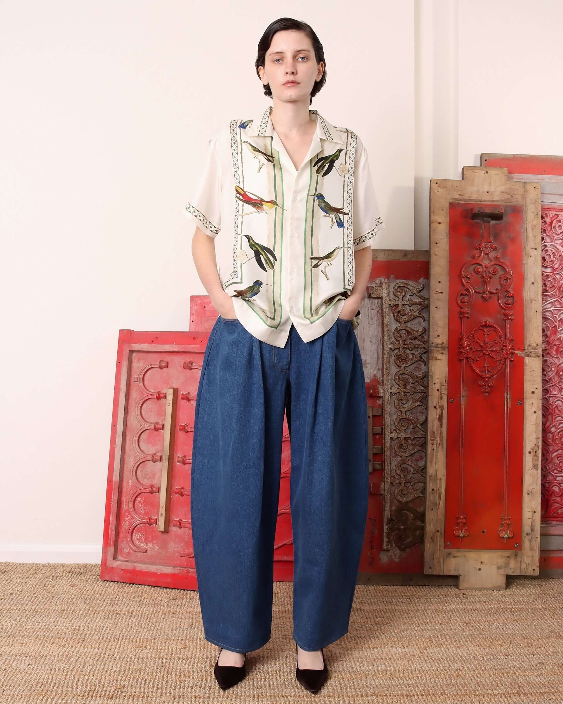 A model wearing the 'Birdwatcher' shirt untucked with her hands tucked into the pockets of denim trousers.