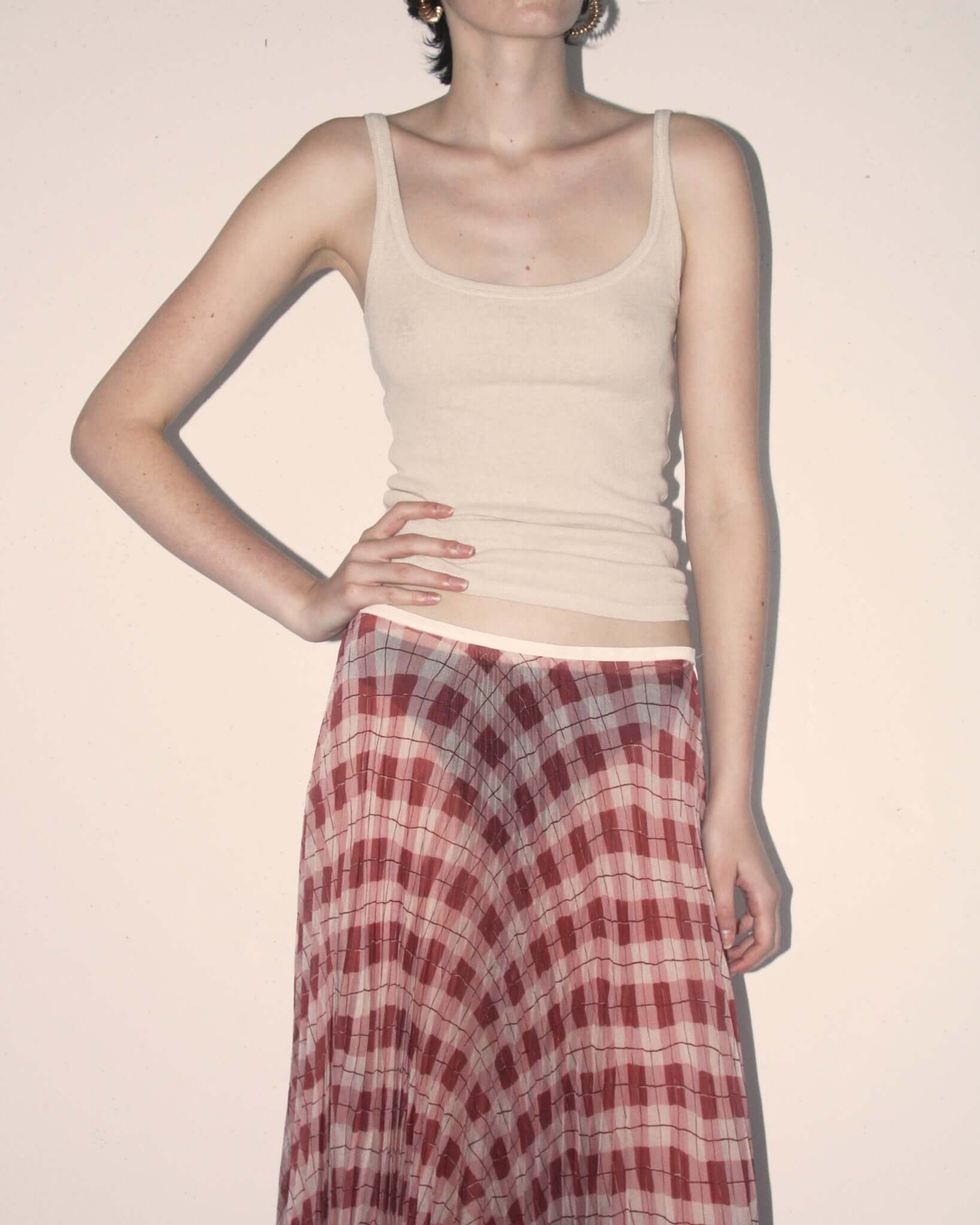 A detail shot of a model wearing the 'Kate' Pleated Skirt in pink argyle and a cream vest.