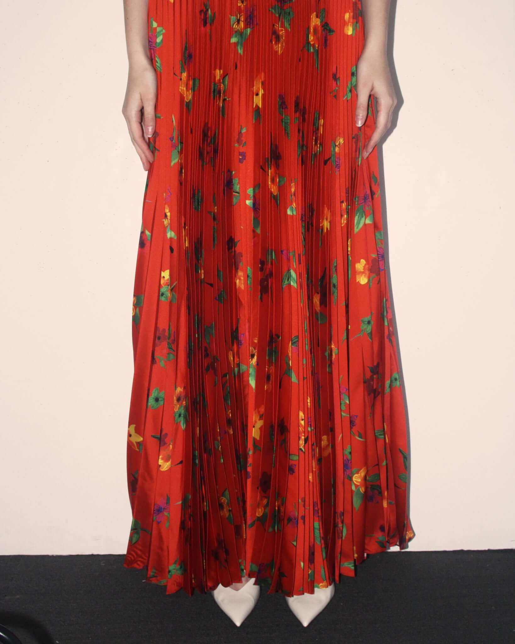 A detail shot of a model wearing the red "Kate' Pleated Skirt and white pointed heels.