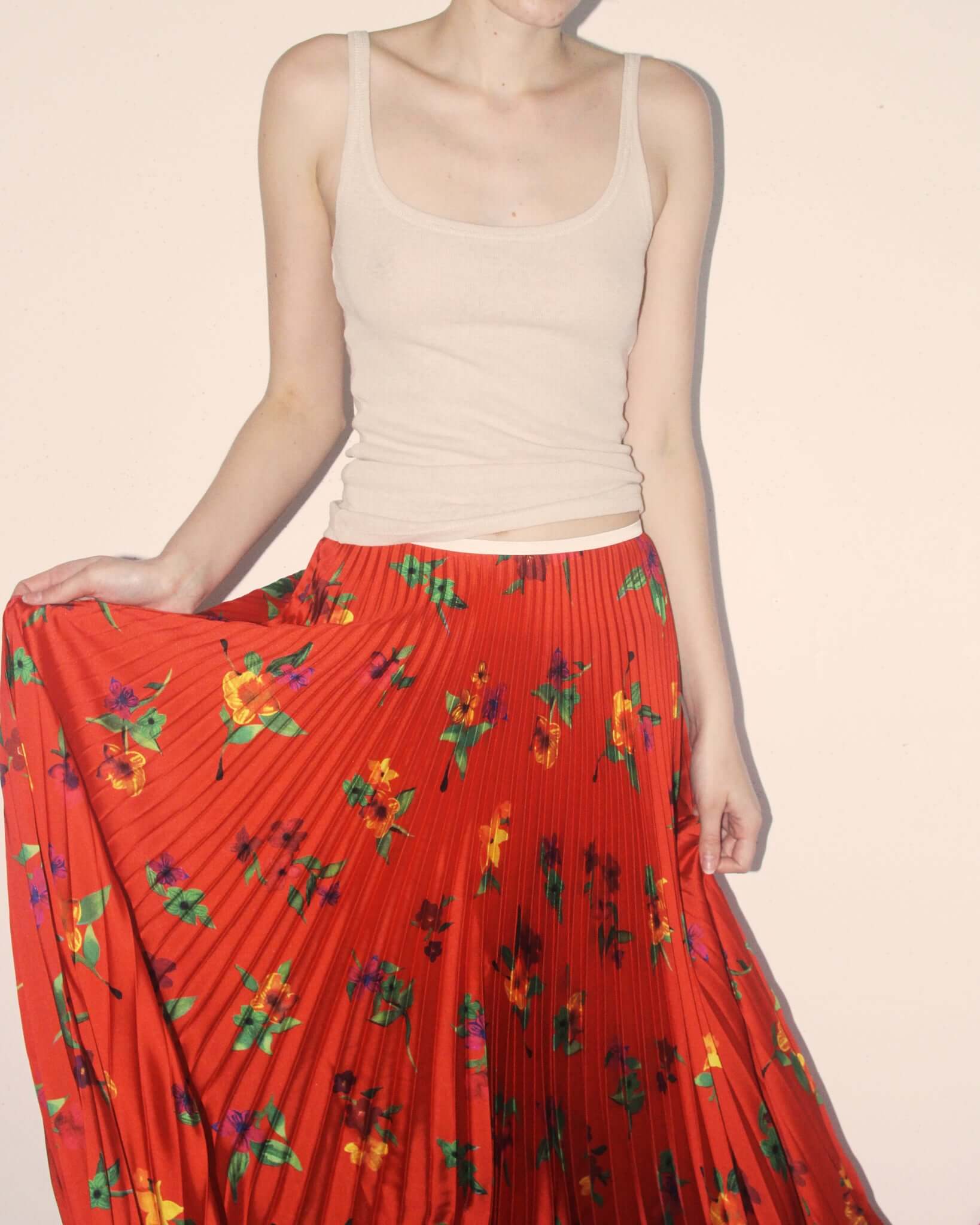 A detail shot of a model creating movement with the pleats of the red 'Kate' Skirt.