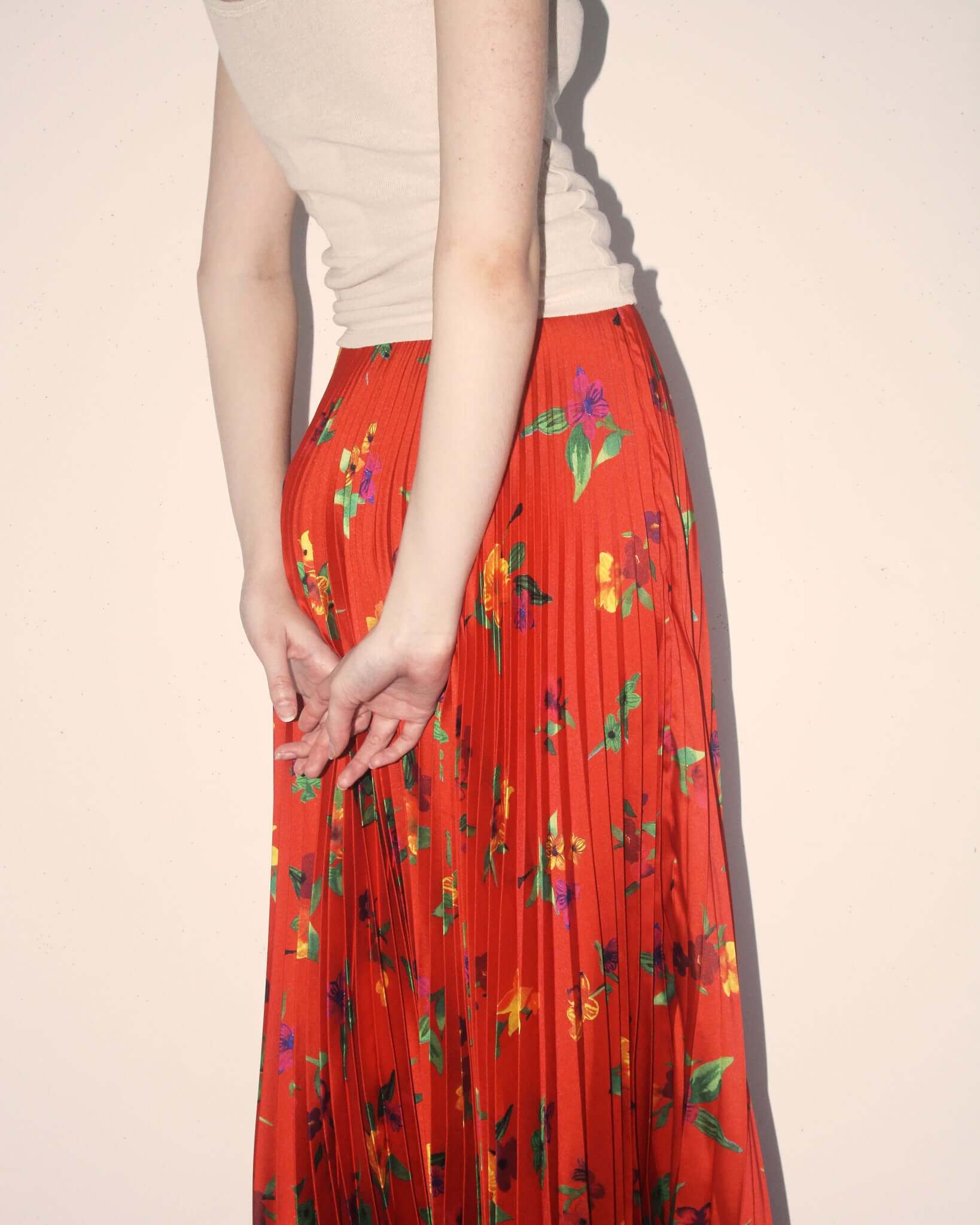 A detail shot of a model wearing the 'Kate' Skirt in colourful yellow, orange, and purple flower and green leaf print on a red base.