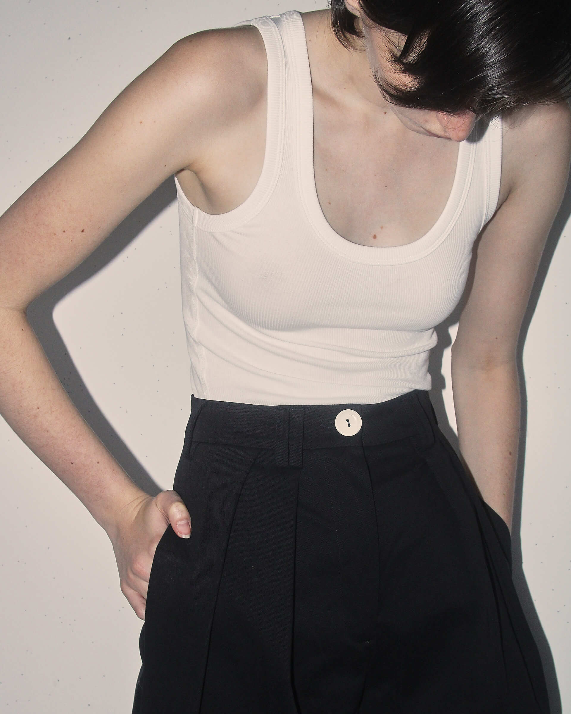 A detail shot of a model wearing the black 'Georgina' Trousers and a white vest.