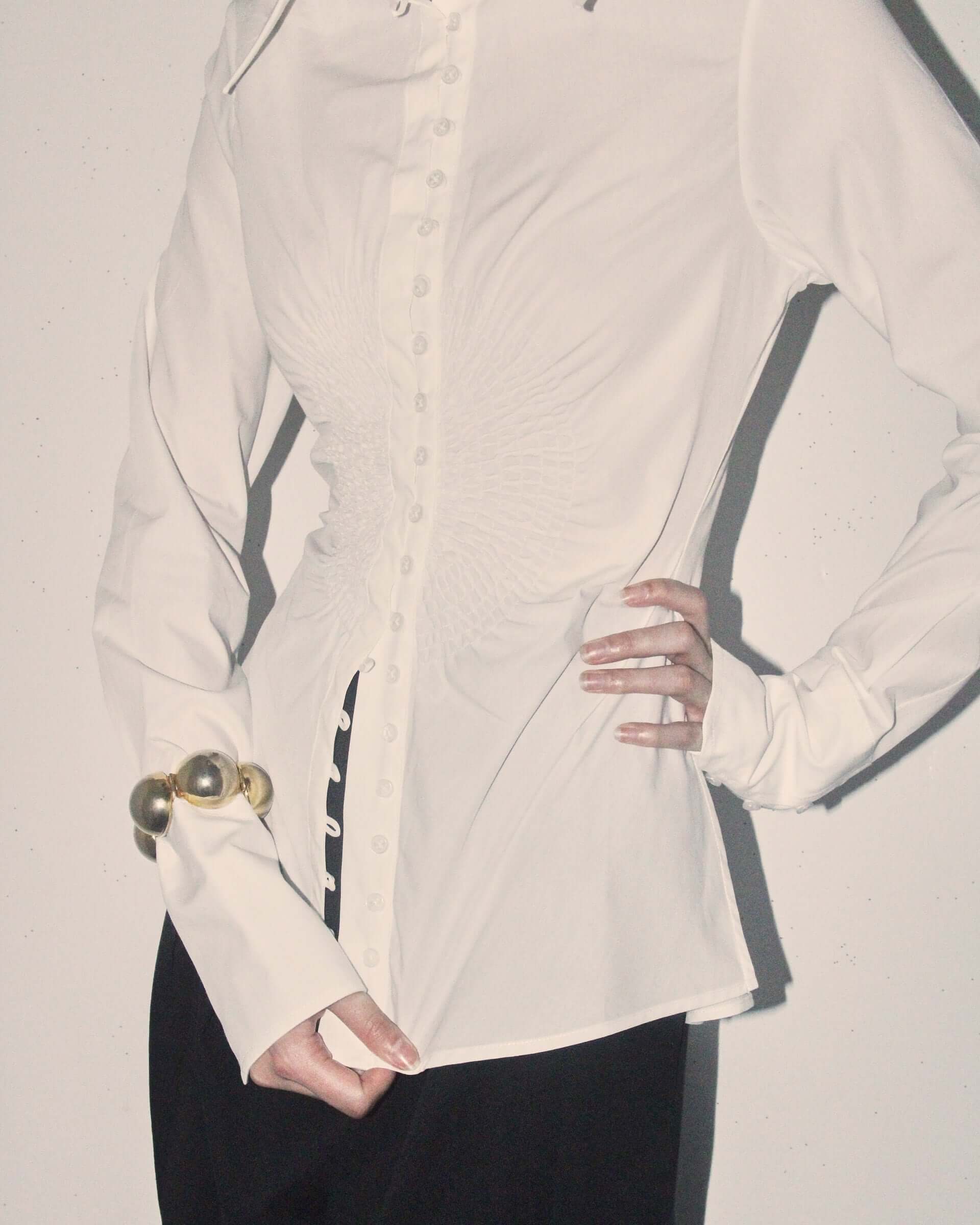 A detail shot of a model wearing the white 'Eva' Circle Shirt and wearing a gold bangle on her wrist.