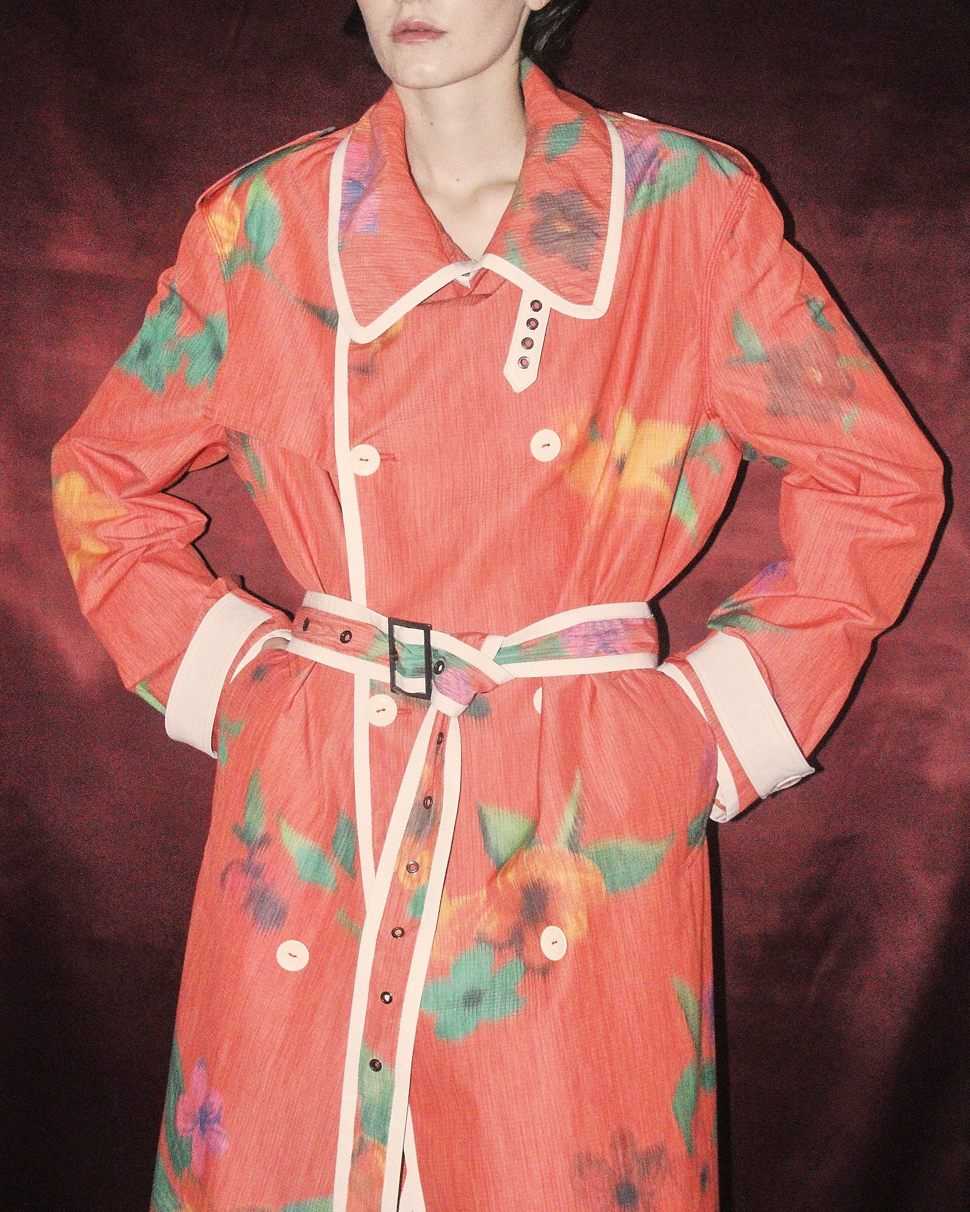 A detail shot of the 'Sophia' Trench in floral print with a light red base, showing the cream lining and attached belt that is tied.