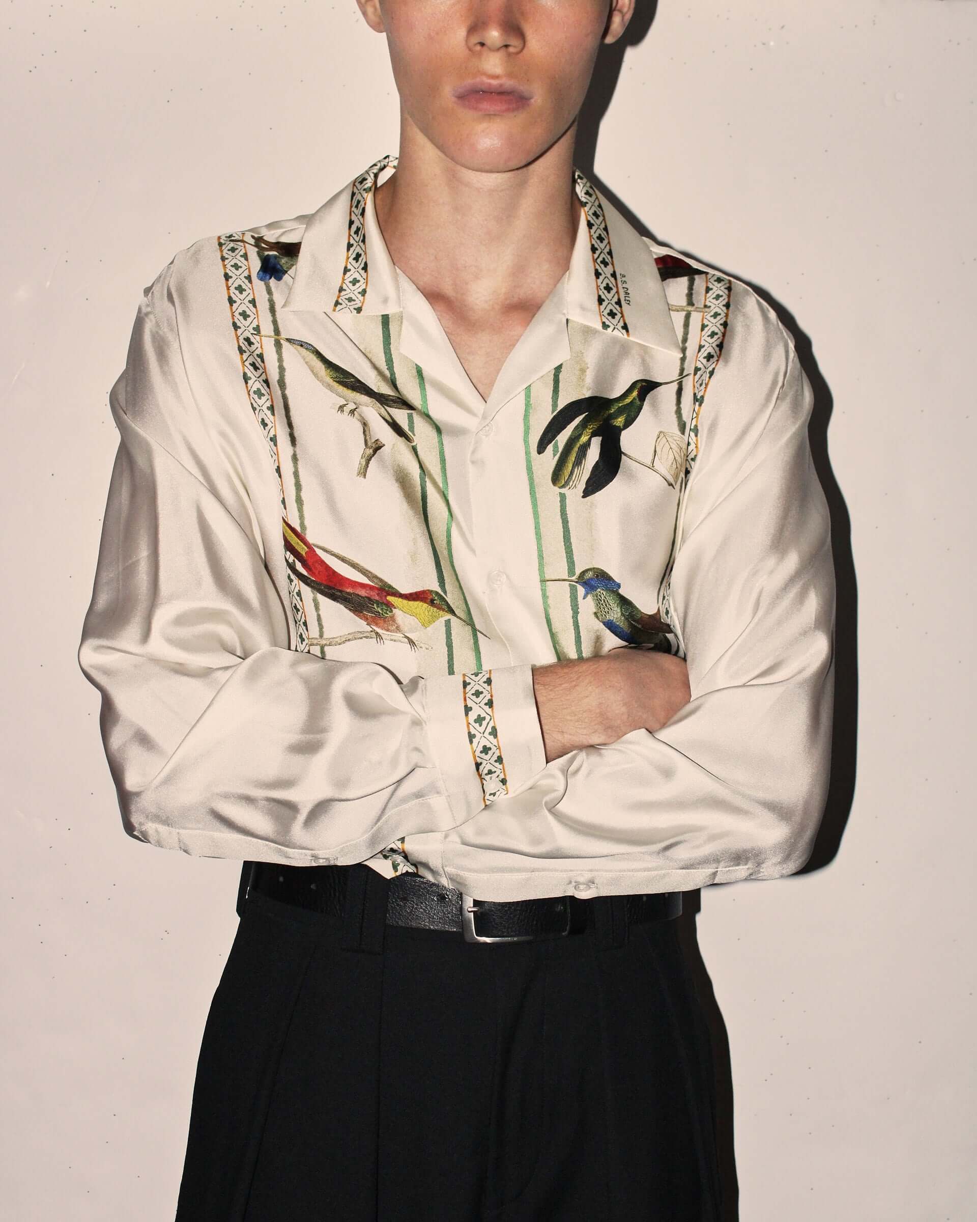 Model wearing a long sleeved silk white shirt with colourful bird embroidery.
