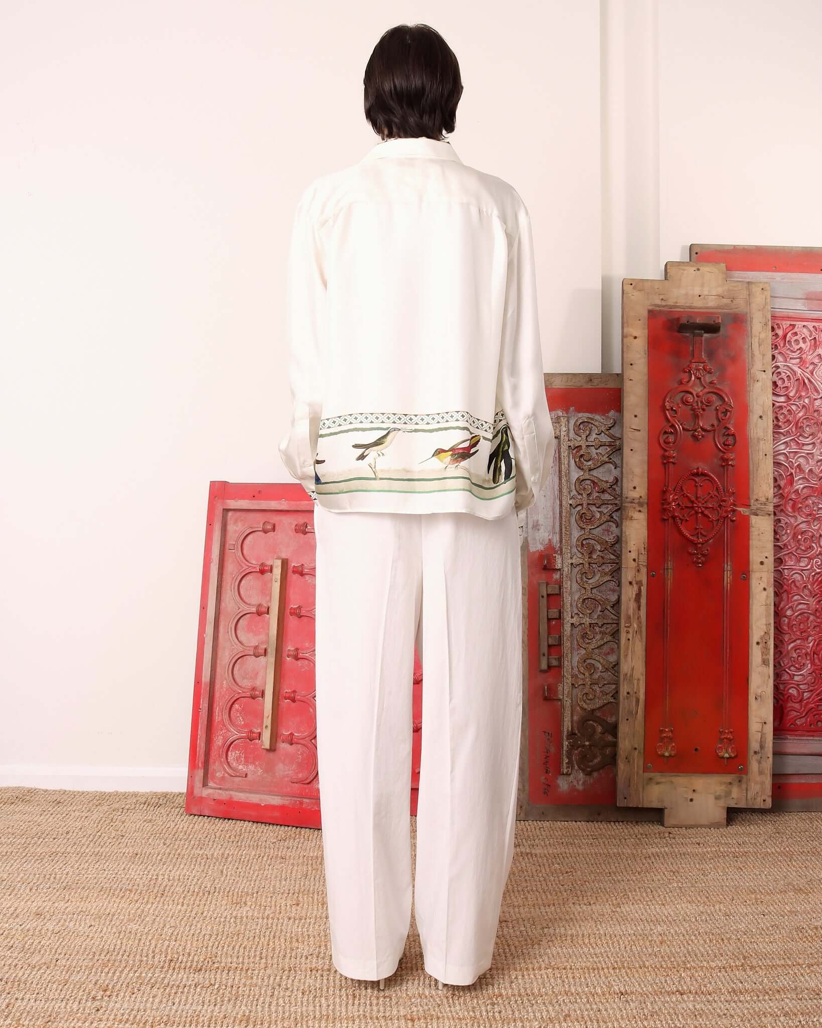 Model wearing the long sleeve 'Birdwatcher' shirt showing the back of the garment and its continued pattern of green weave and stripe designs with hummingbirds across the bottom of the shirt.