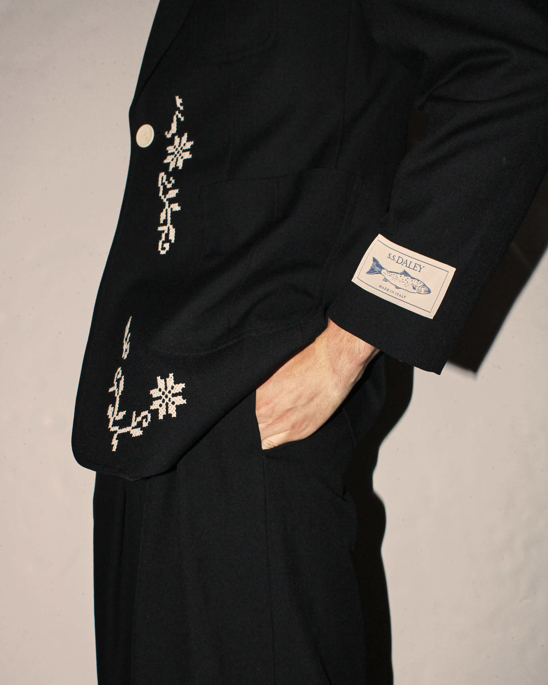 A close-up of the 'Albert' Jacket and it's white floral embroidery along the hemlines, as well as a signature S.S.DALEY 'Made in Italy' patch on the sleeve above the cuff.