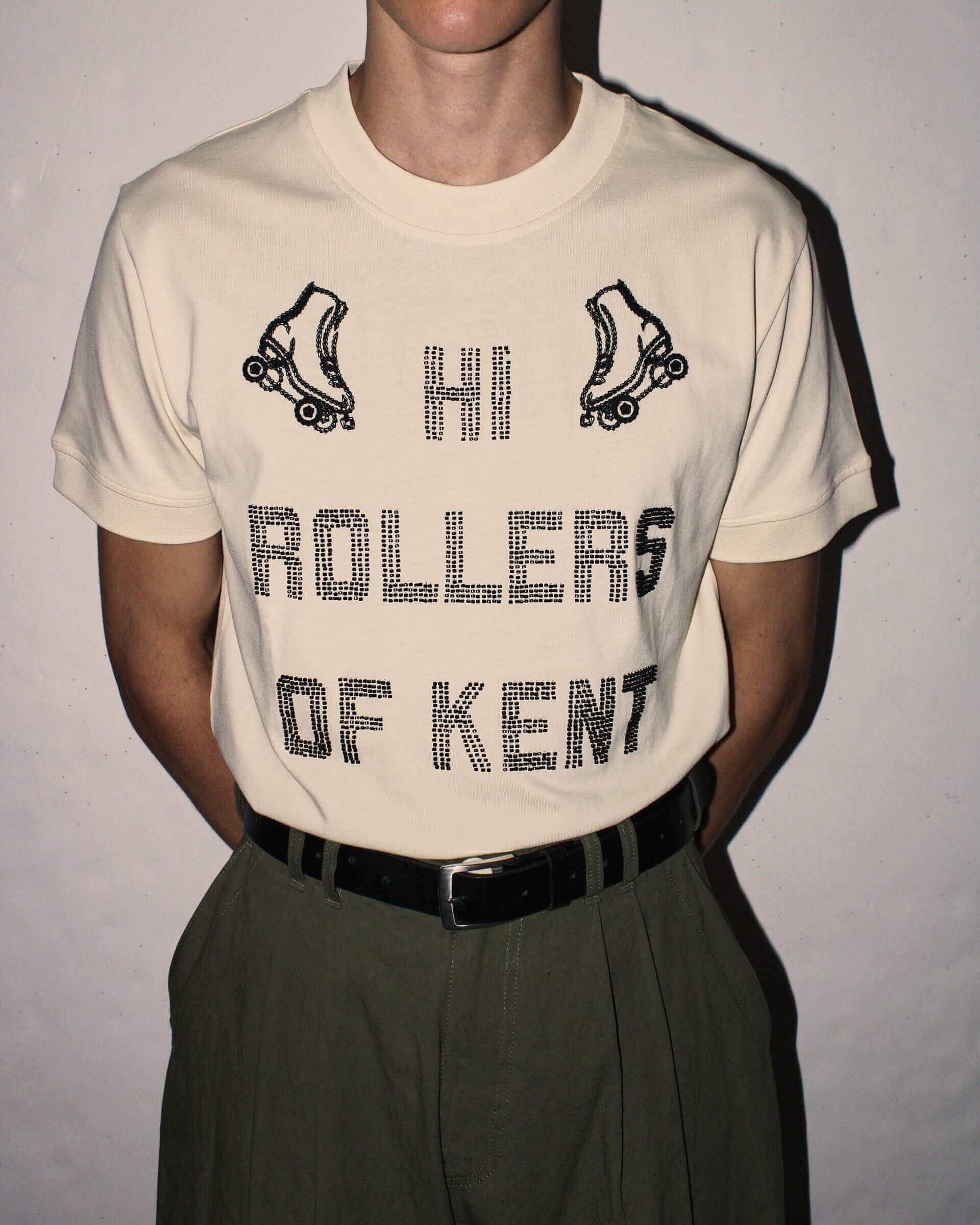 Model wearing an ecru  t-shirt with black 'Hi Rollers of Kent' text and roller skate graphics.