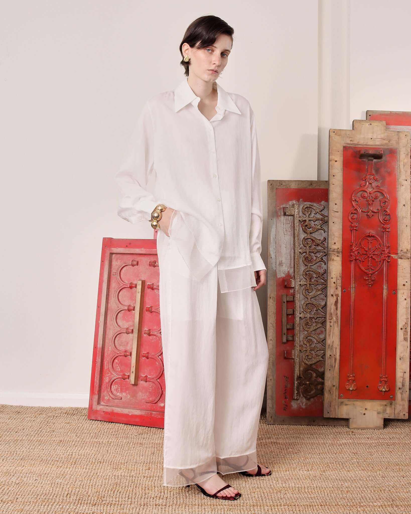 Model wearing the white 'Orla' long sleeve  shirt and the matching white 'Olra' trousers with one hand in the pocket and the shirt untucked.
