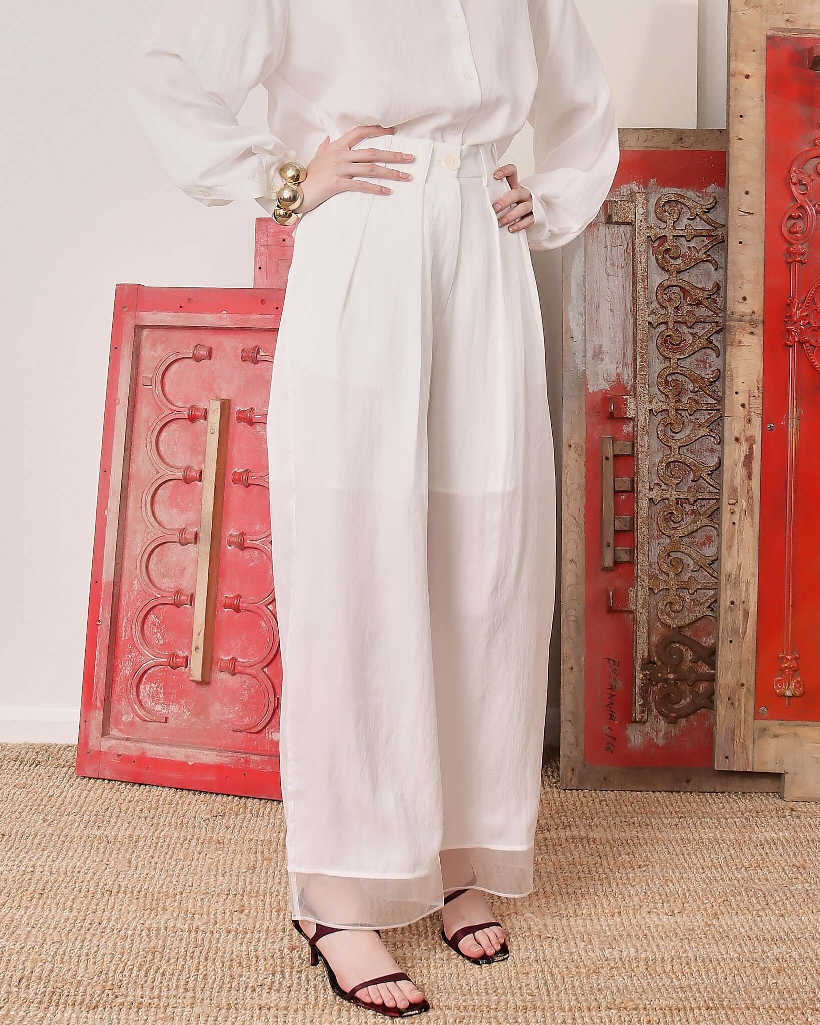 A close-up of a model wearing the white 'Orla' Trousers, showing the intricate pleating, breathable fabric, and delicate organza hem. 