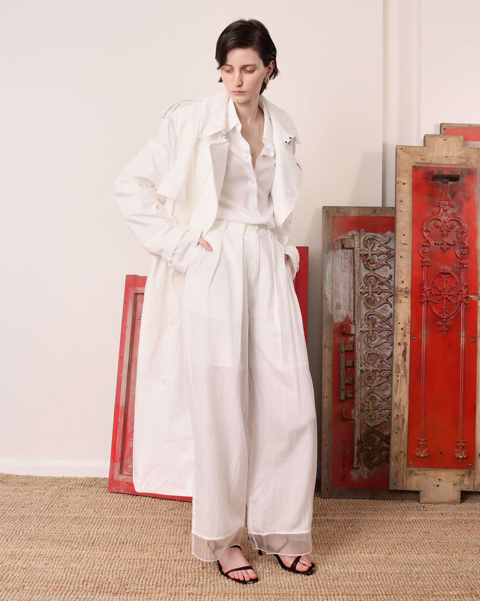 A model poses with the 'Sophia' Trench unbuttoned and paired with a matching set of a white shirt and white trousers underneath.