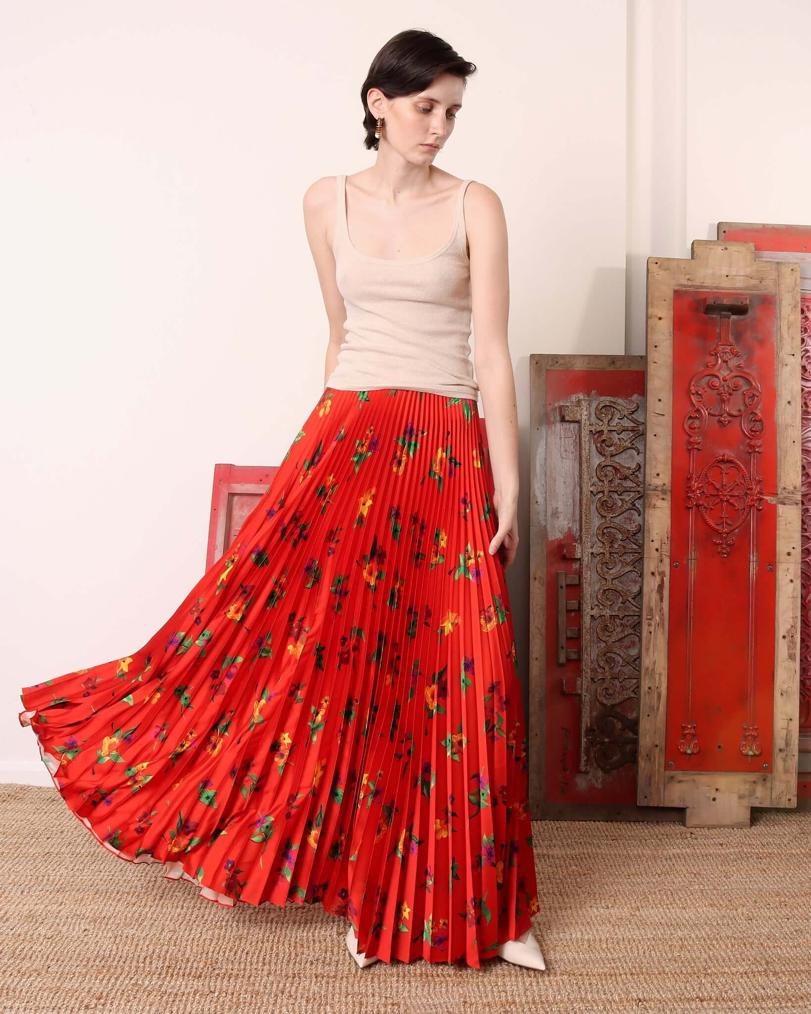 A model wears the 'Kate' Pleated Skirt in red showing the movement of the pleats and floor-length.