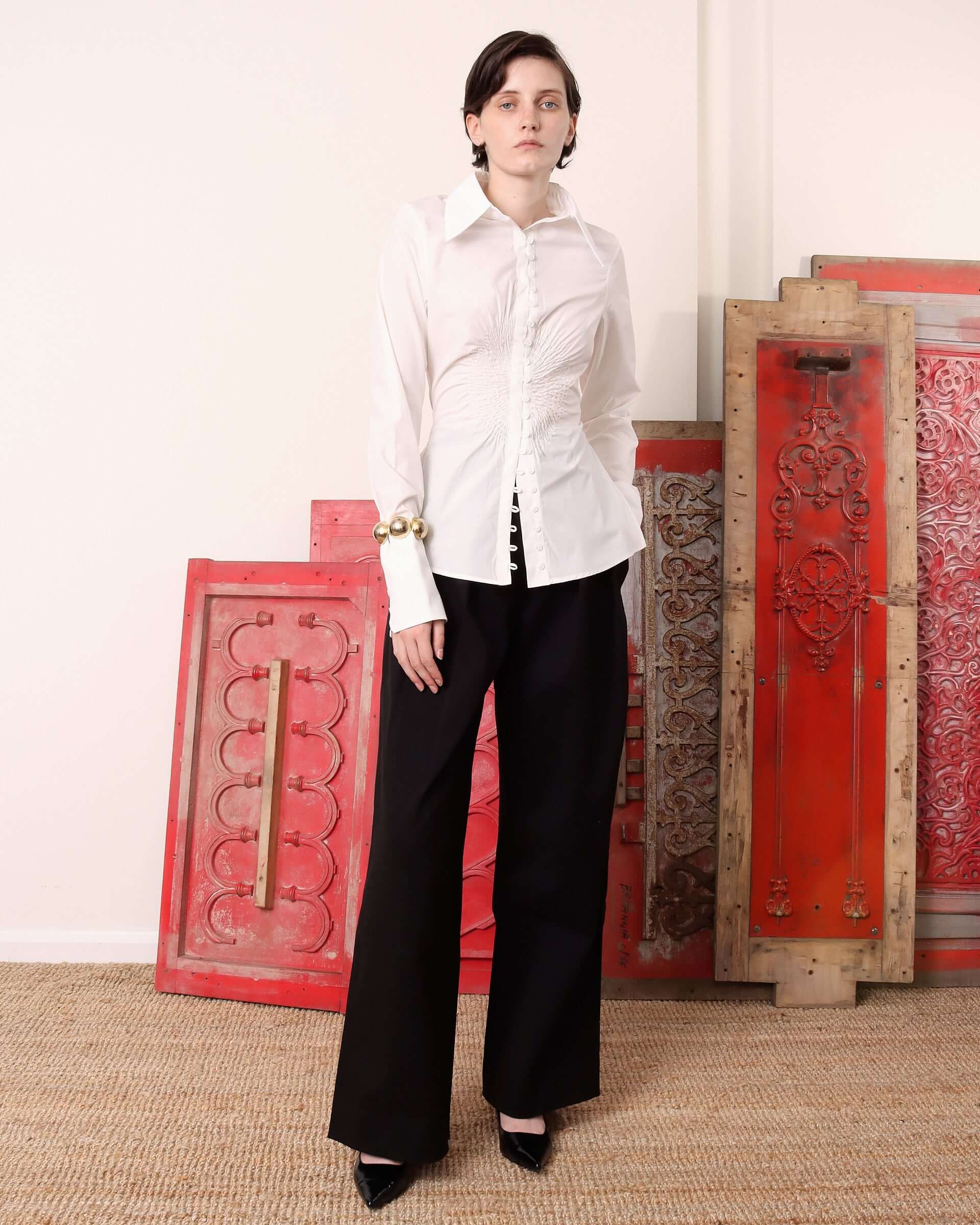 A model wears the 'Eva' Circle Shirt in white untucked with a pair of black trousers.