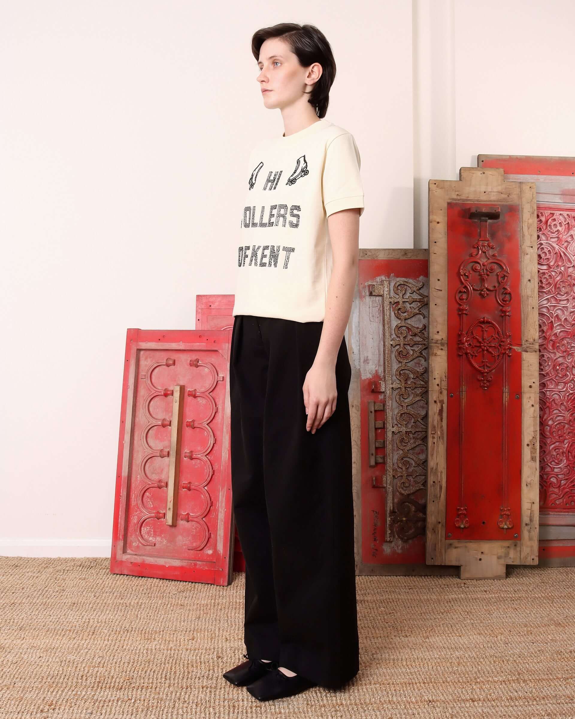 A model wearing the ecru 'Hi Rollers' T-shirt and matching black trousers.