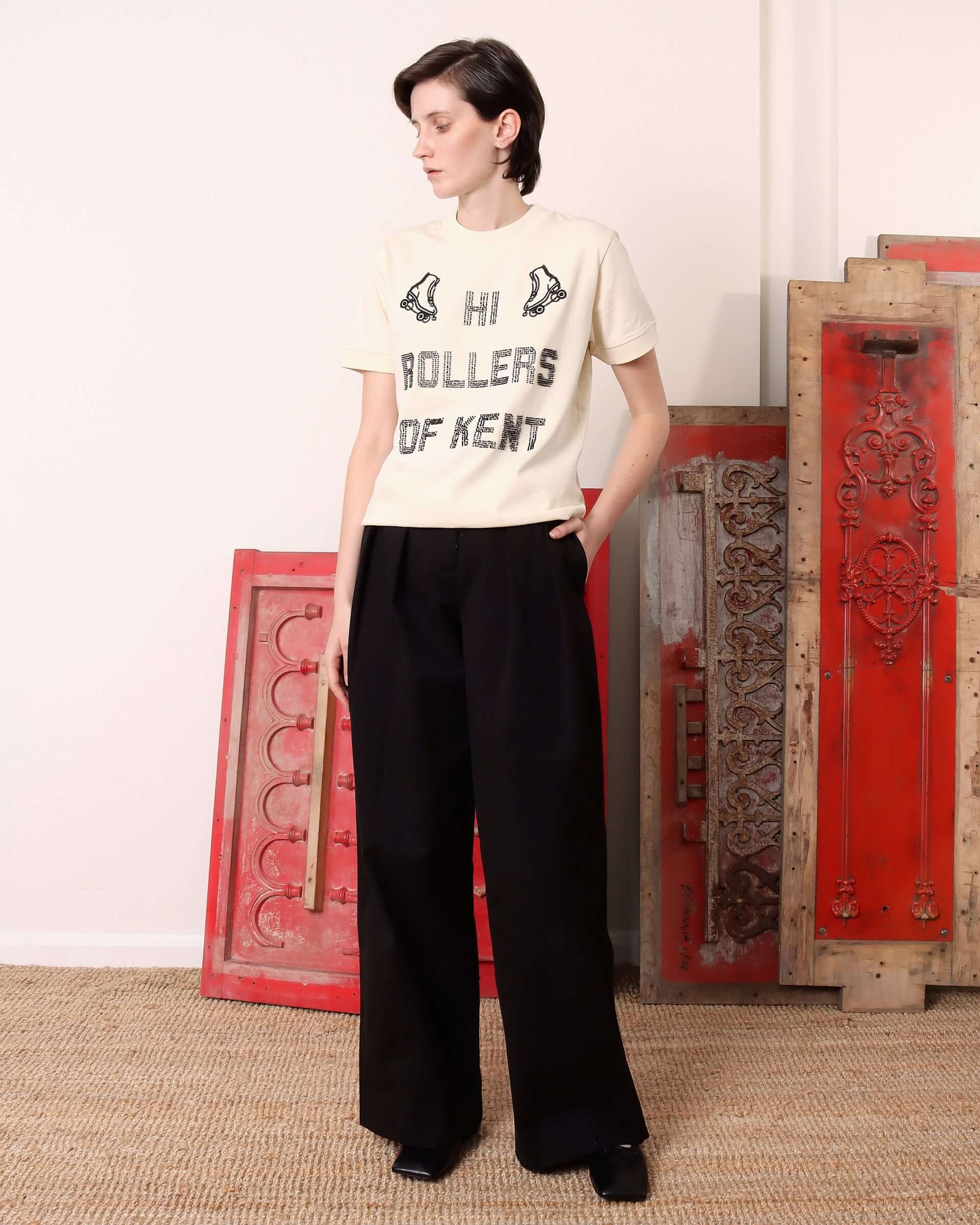 Model wearing the 'Hi Rollers' T-shirt in Ecru with black beading reading 'Hi Rollers of Kent'  across the front and two embroidered roller skates on either side.