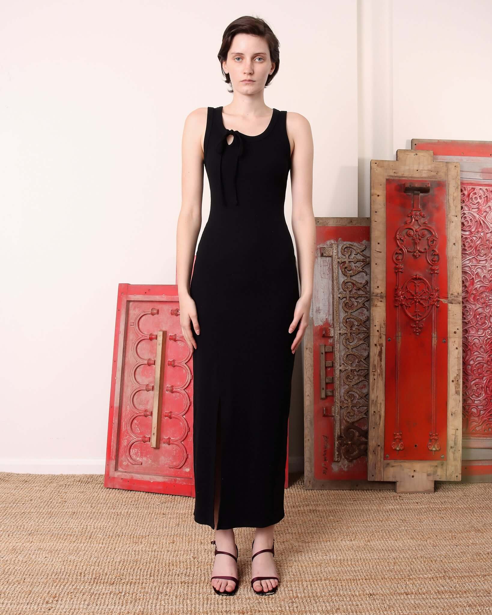 A model wears the 'Lila' Jersey Dress in black. The maxi dress has a slit hem and asymmetric tie detail at the neckline.