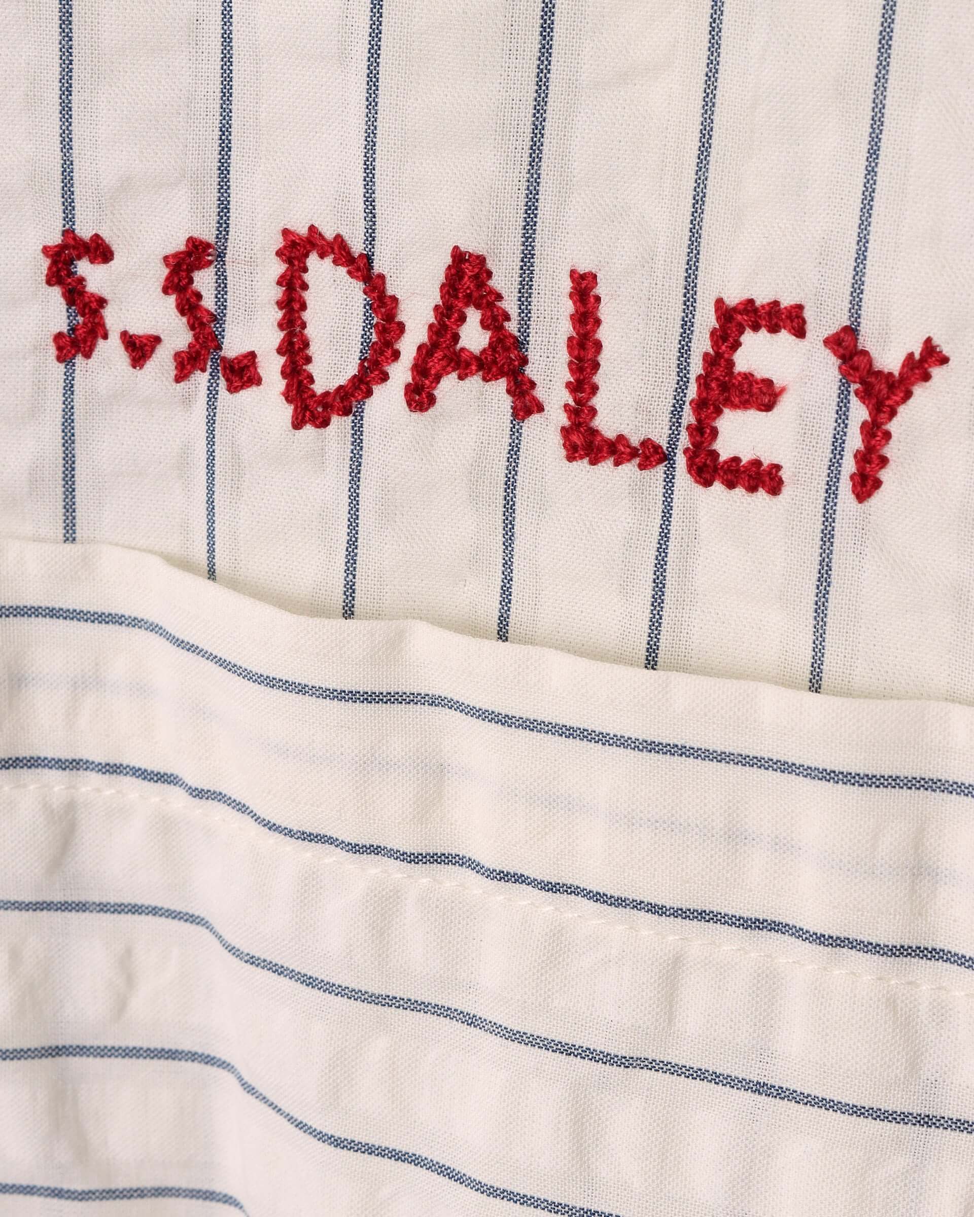 A close-up of the red stitched S.S.DALEY logo and the seersucker fabric with light blue stripes on a white base.