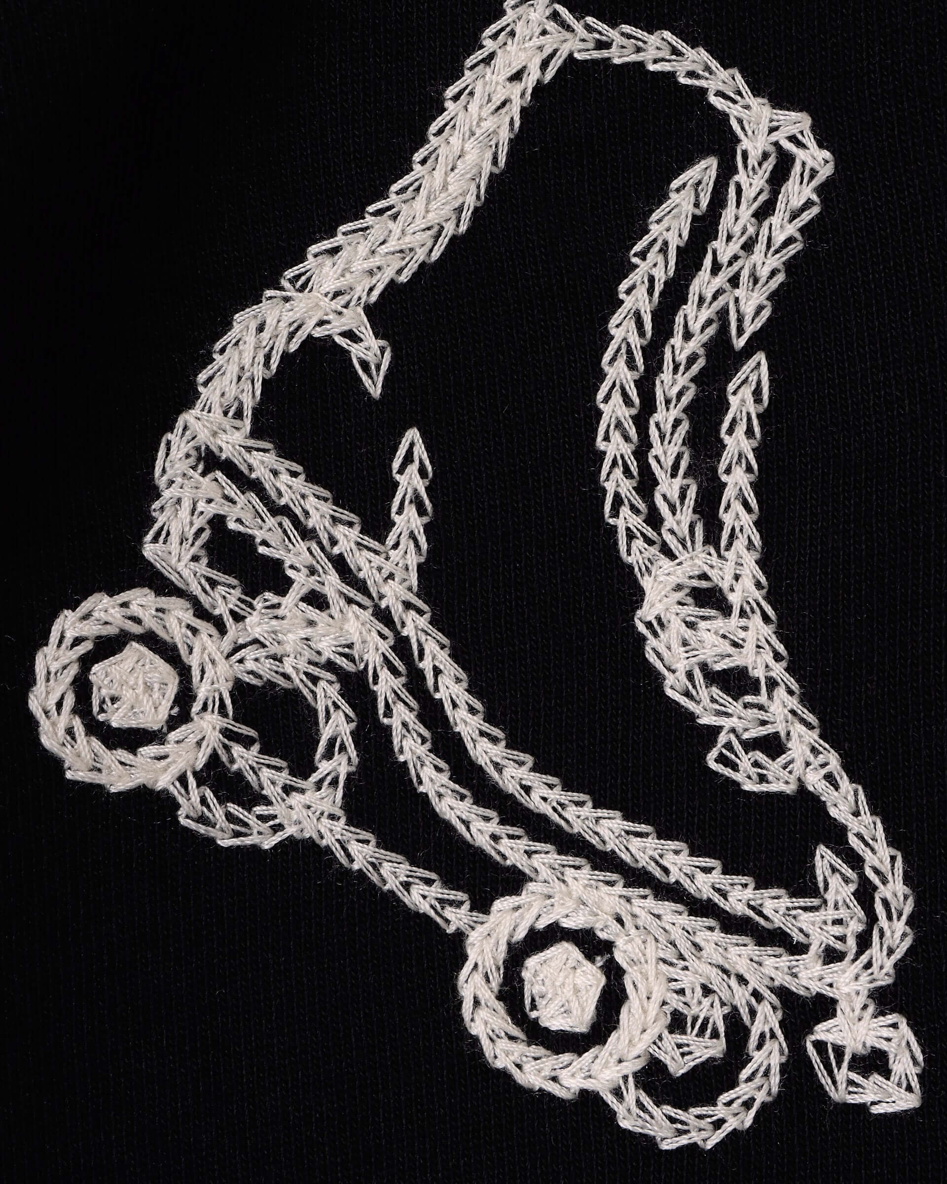 A close-up of an embroidered ecru roller skate on a black jersey background.