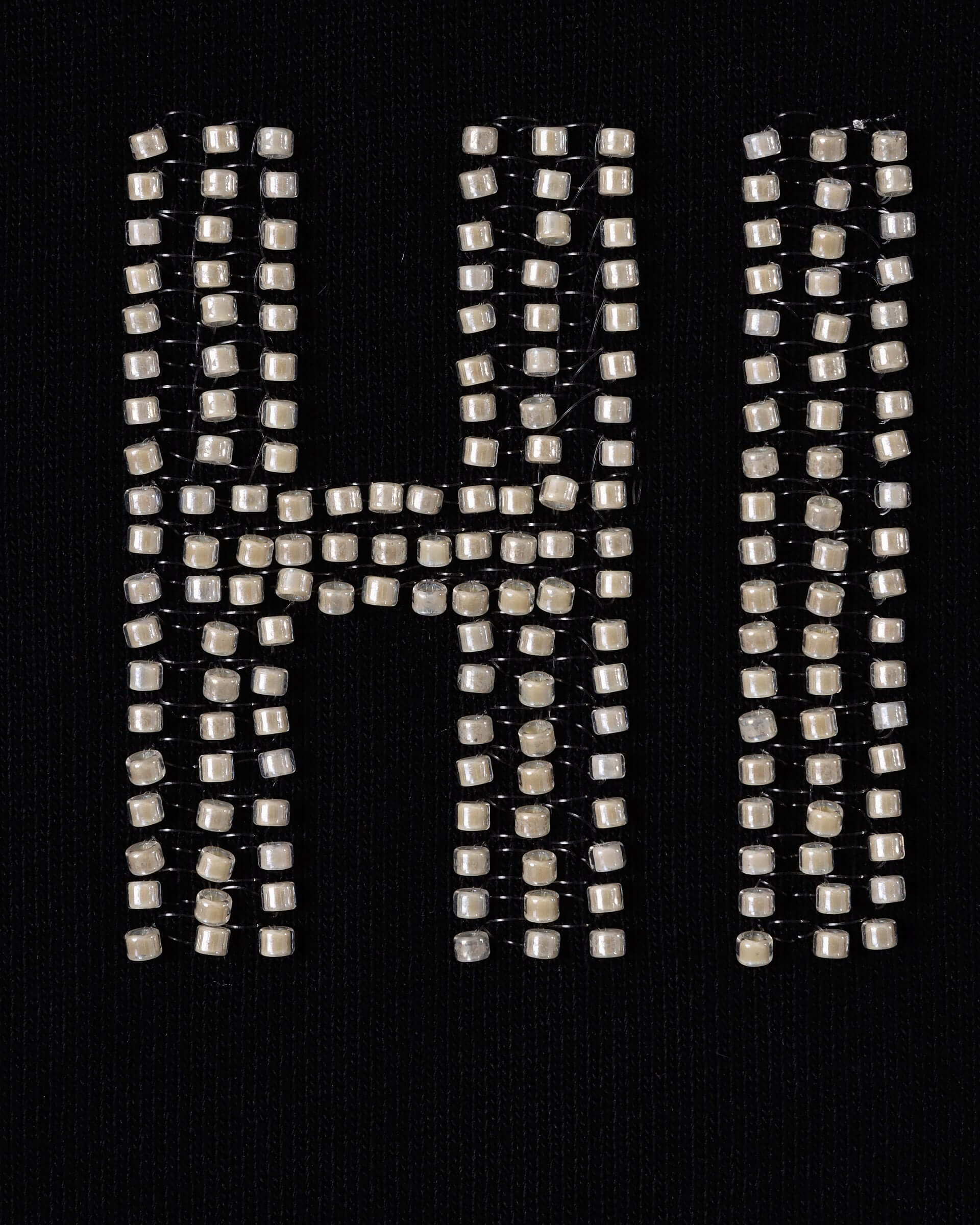 A close up of the intricate beading for the tee's slogan on the black jersey background.