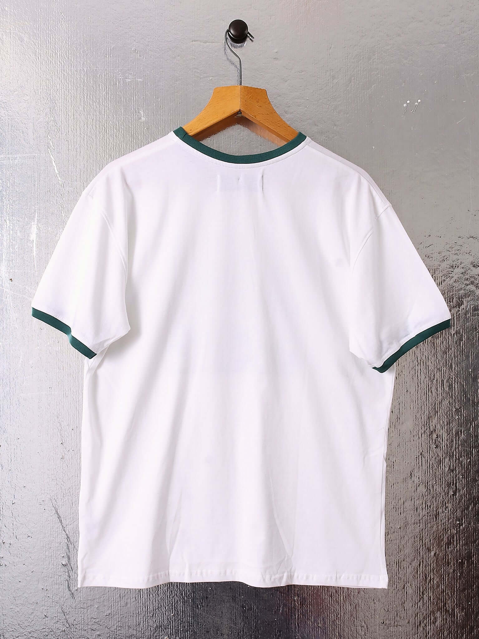 A flat shot of the back of the white 'Garden Block' Printed T-Shirt showing the white back and thin green piping that continuous on the sleeve cuffs and neckline.