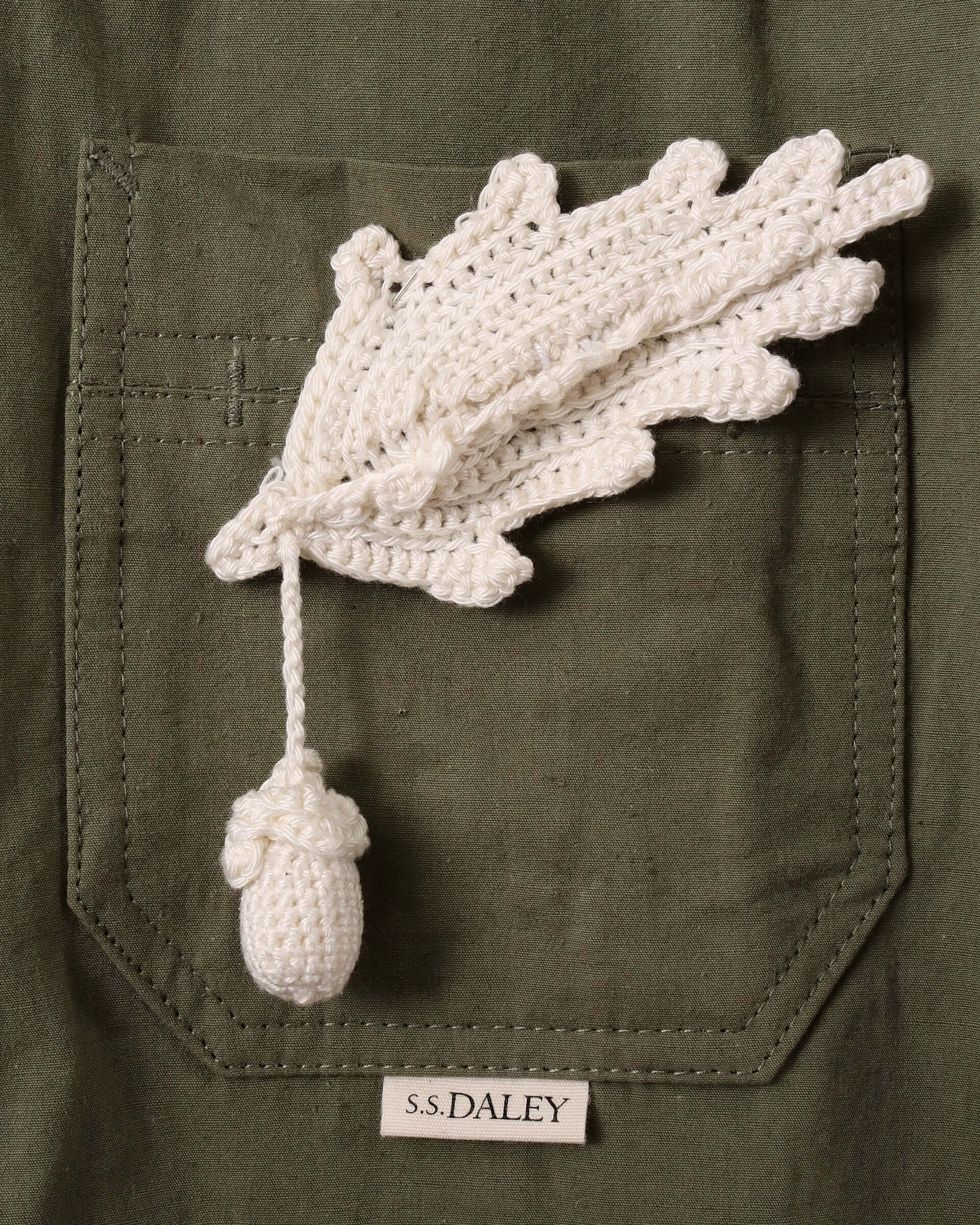 A close-up of the front chest pocket with the detachable white hand-crocheted acorn pin and small S.S.DALEY logo just under the pocket.