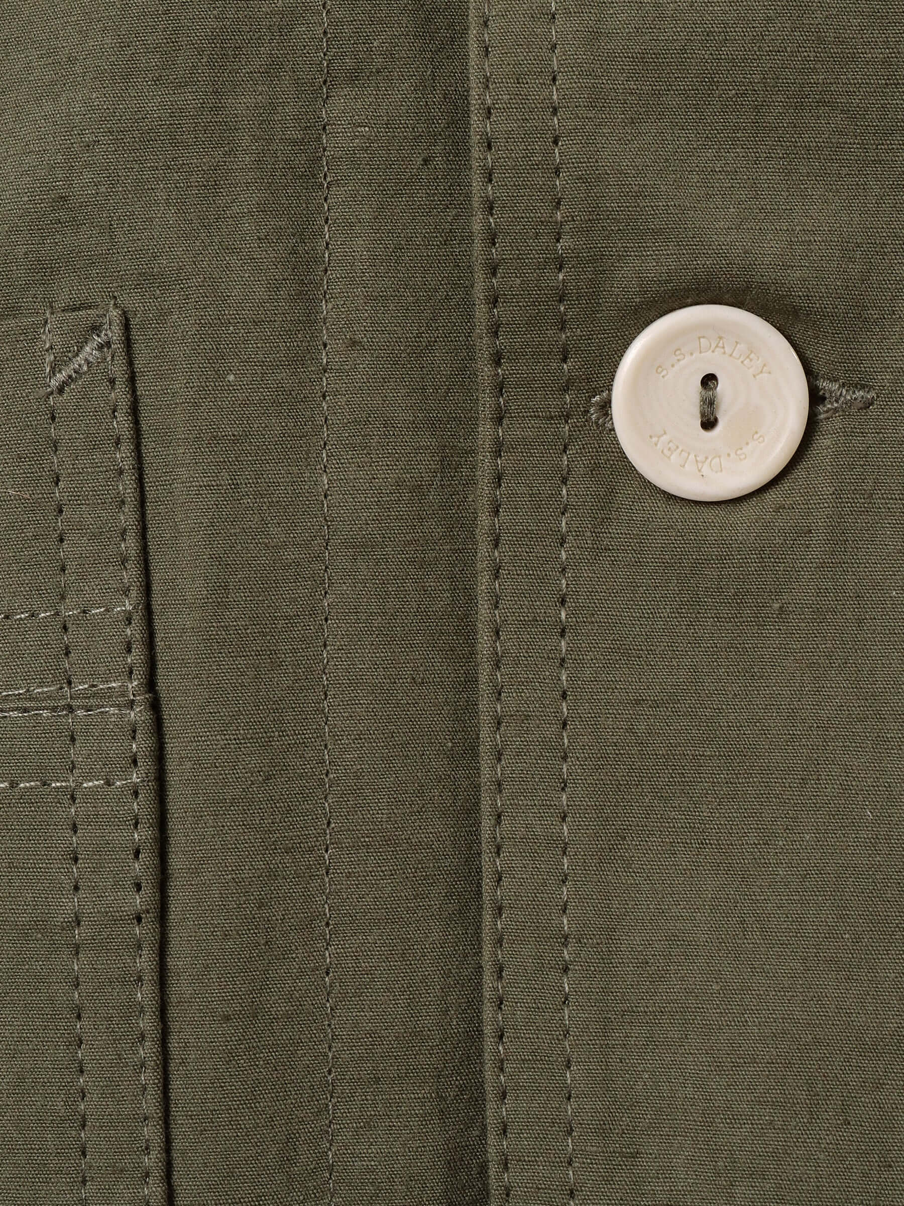 A close up of the technical Japanese cotton-blend fabric and seams as well as an Ecru button engraved with S.S.DALEY on the green 'Clarence' Chore Jacket.
