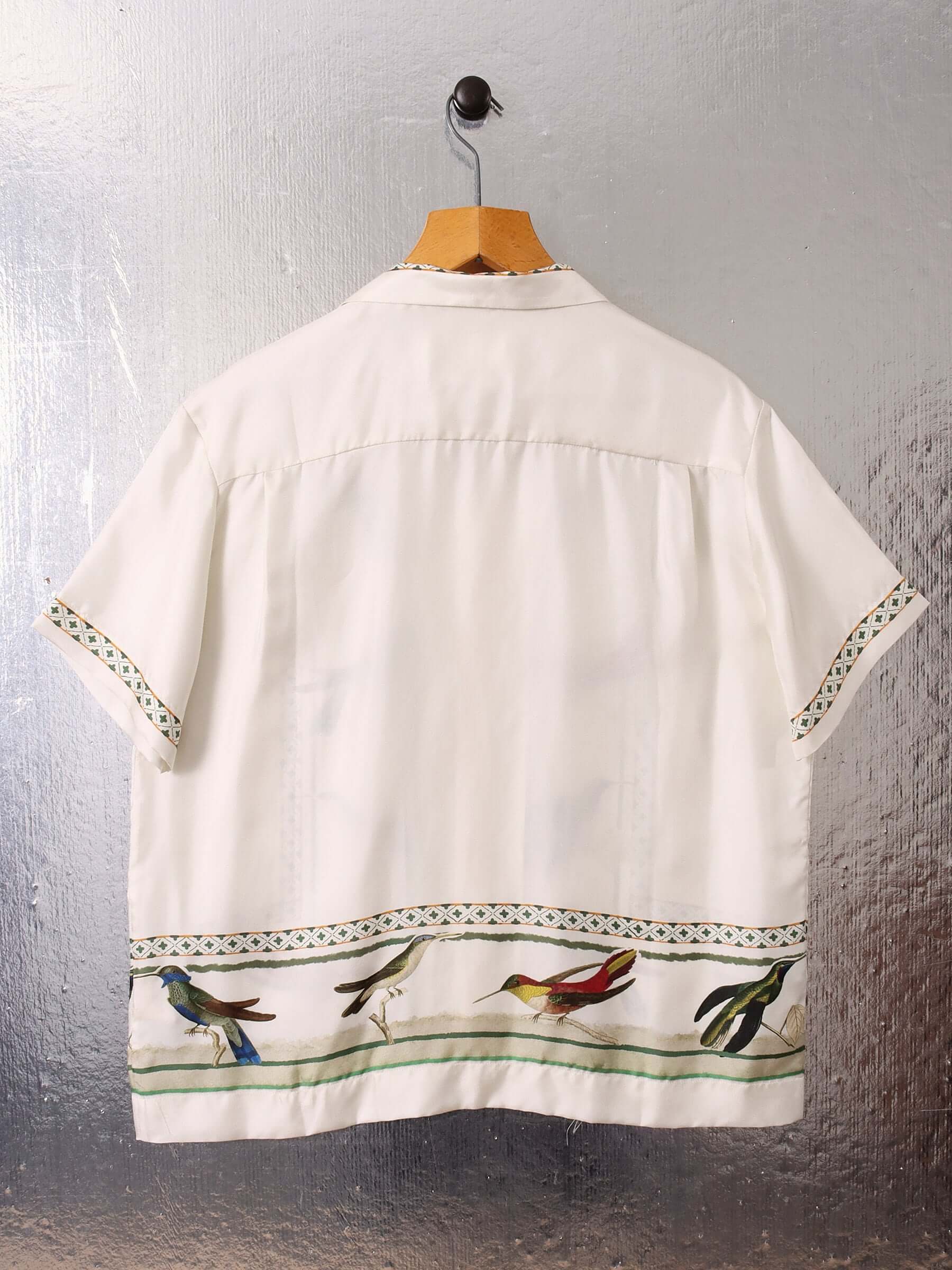A flat detail shot of the 'Birdwatcher' shirt on a hanger, showing the back of the garment and the continuation of the bird and green weave and stripe pattern along the bottom.