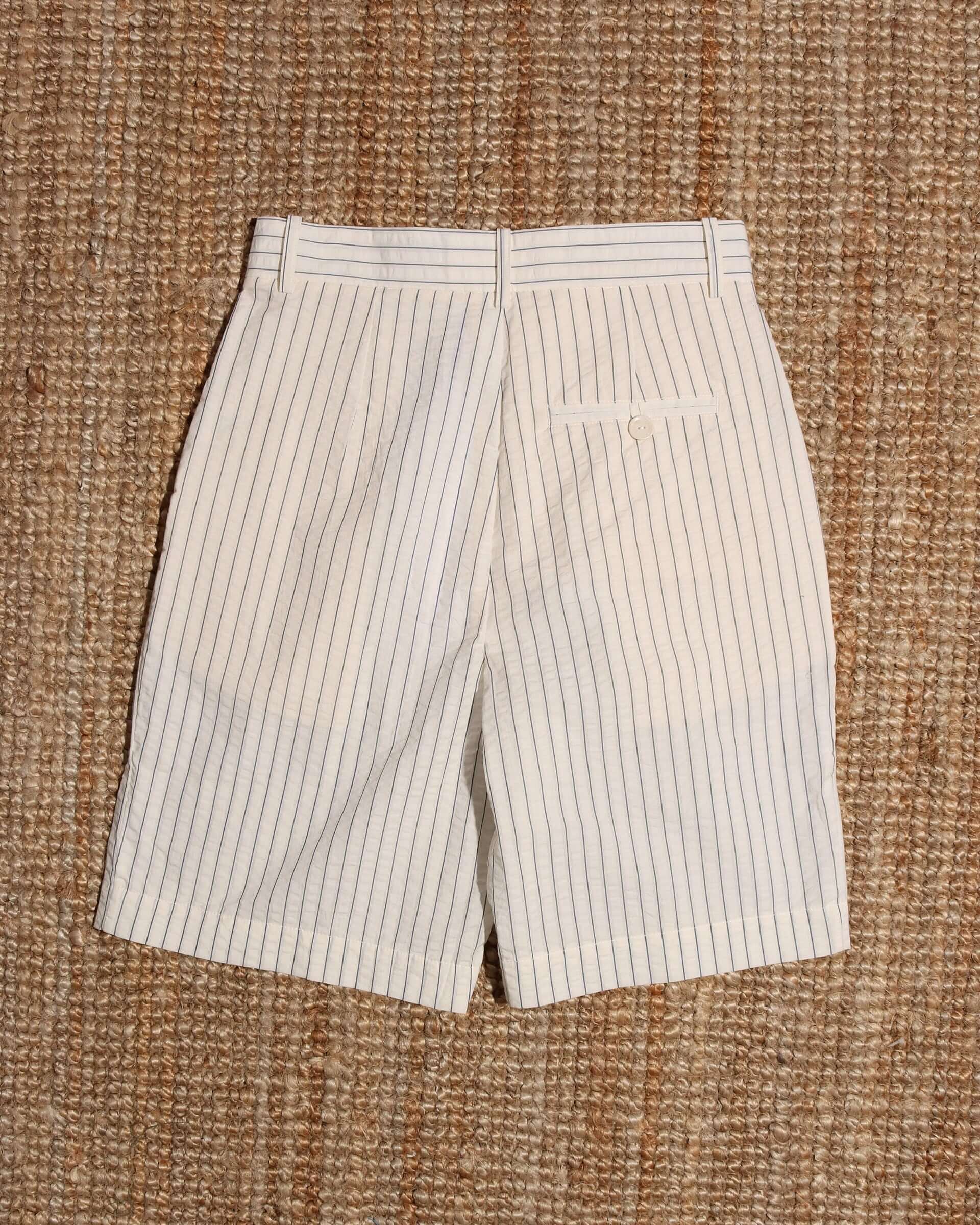 A flat shot of the back of the 'Clement' Shorts showing the mid-rise waist and white with blue pinstripes seersucker fabric.