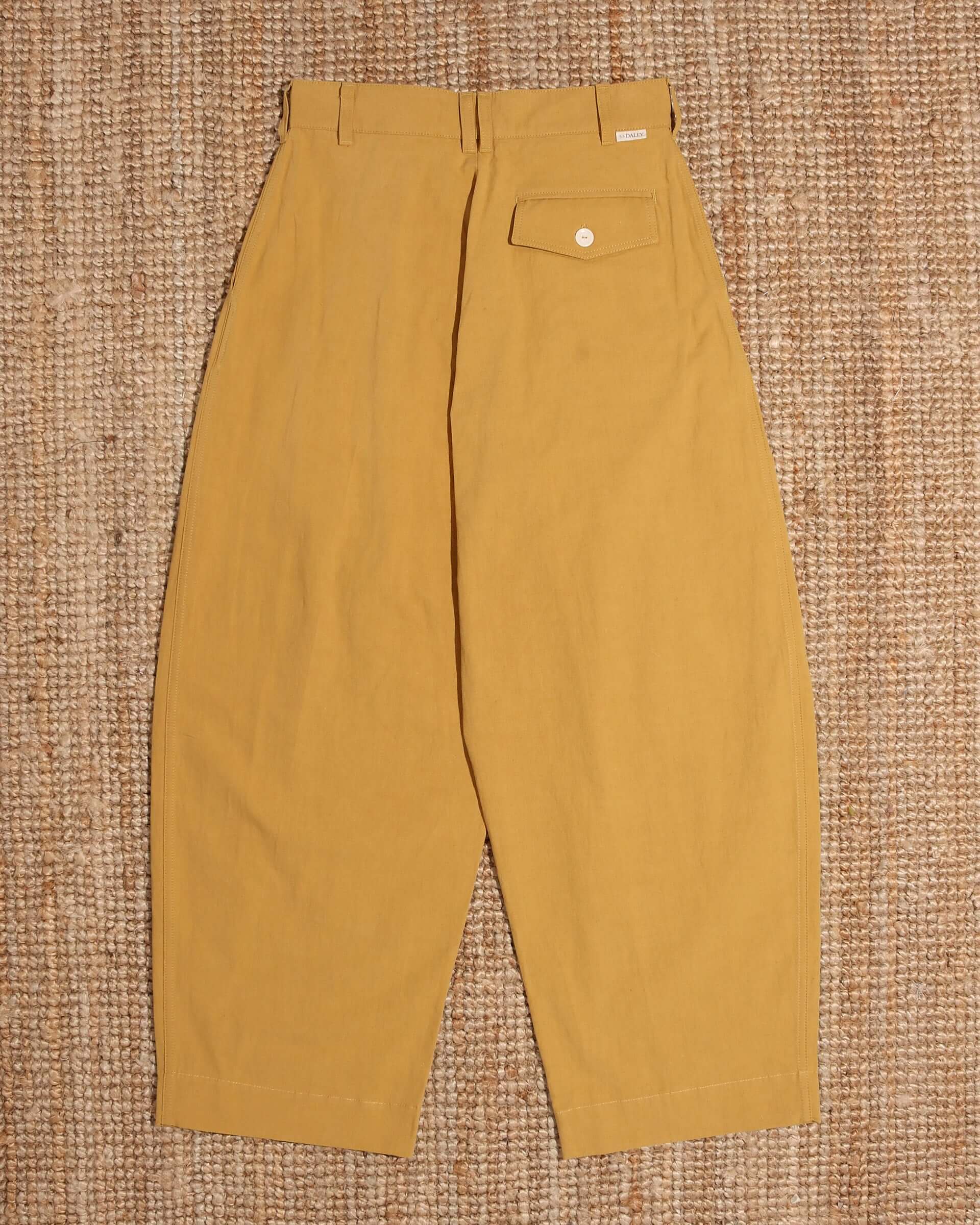 A flat shot of the back of the 'Clarence' Trouser in mustard, showing the rounded leg stye and the back pocket with the S.S.DALEY engraved white button.