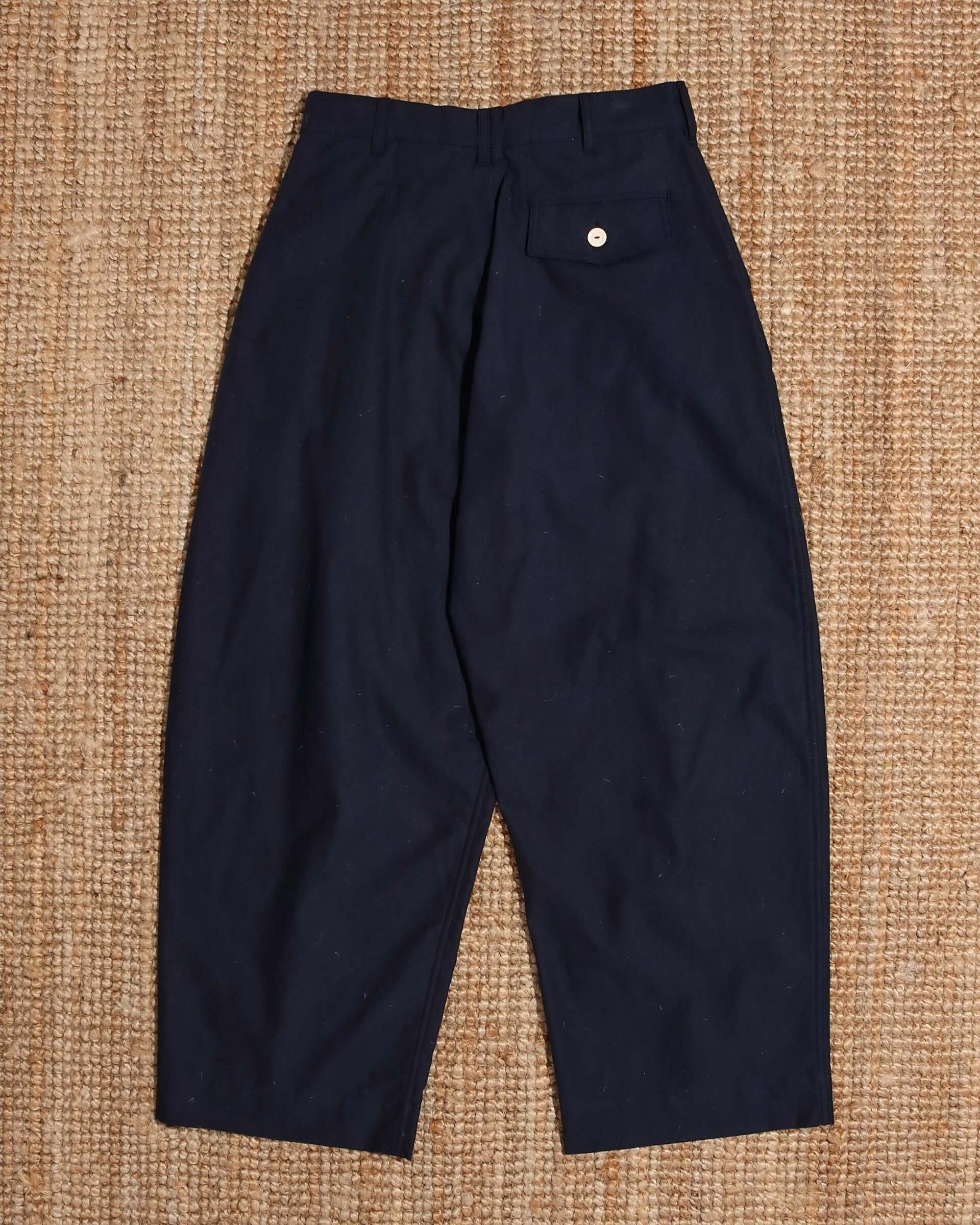A flat shot of the back of the 'Clarence' Trousers in navy, showing the rounded legs and white button pocket closure.
