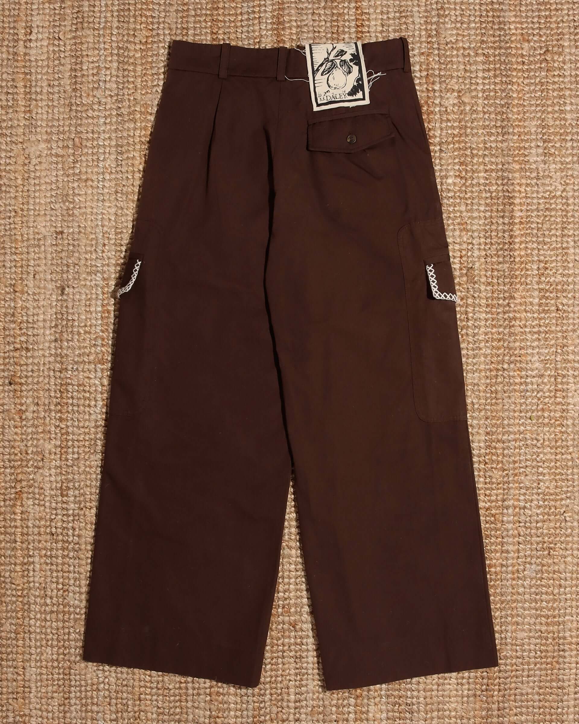A flat shot of the 'Milton' Cargo Trouser in brown showing the S.S.DALEY label near the waist with a black pair print on a cream background.