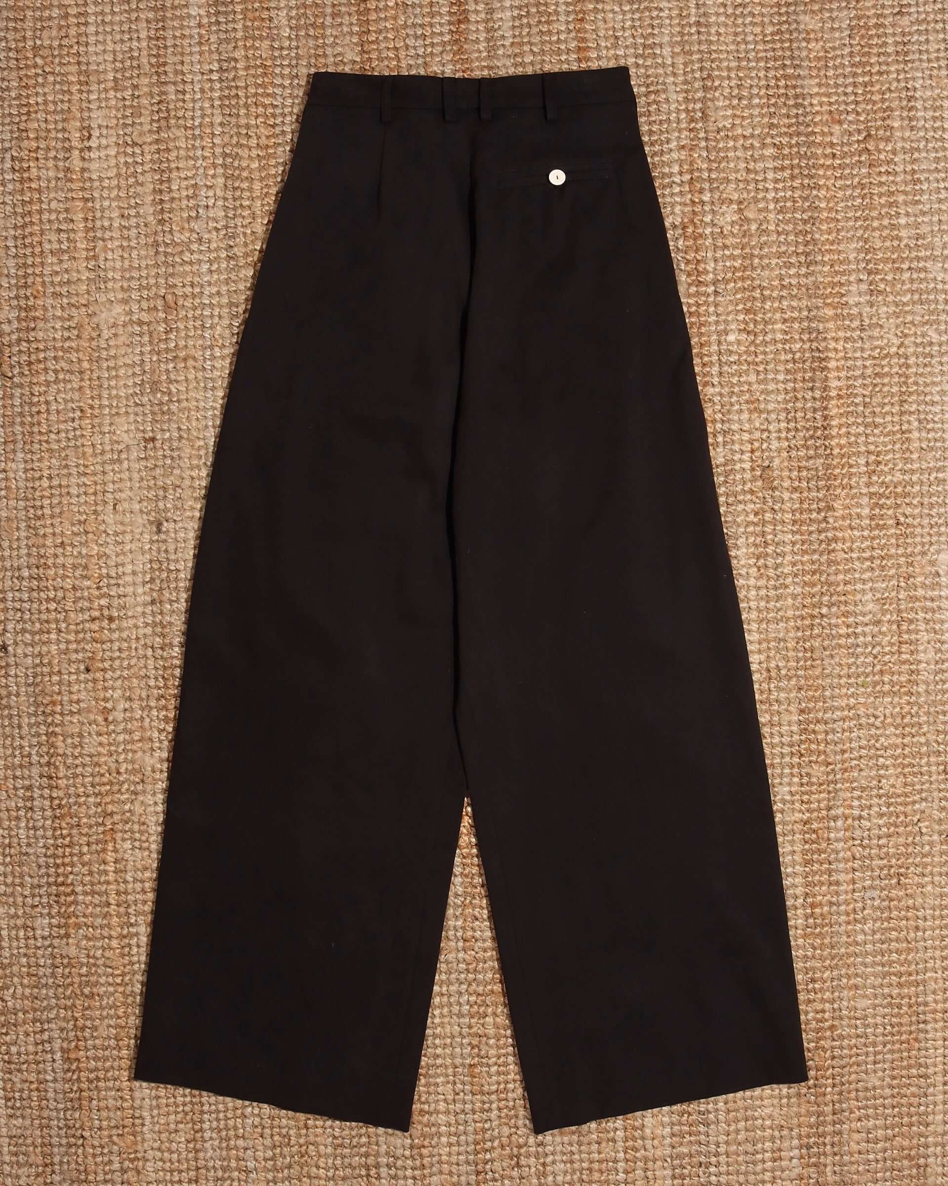A flat image of the back of the black 'George' Trouser and its back pocket with a white button closure.