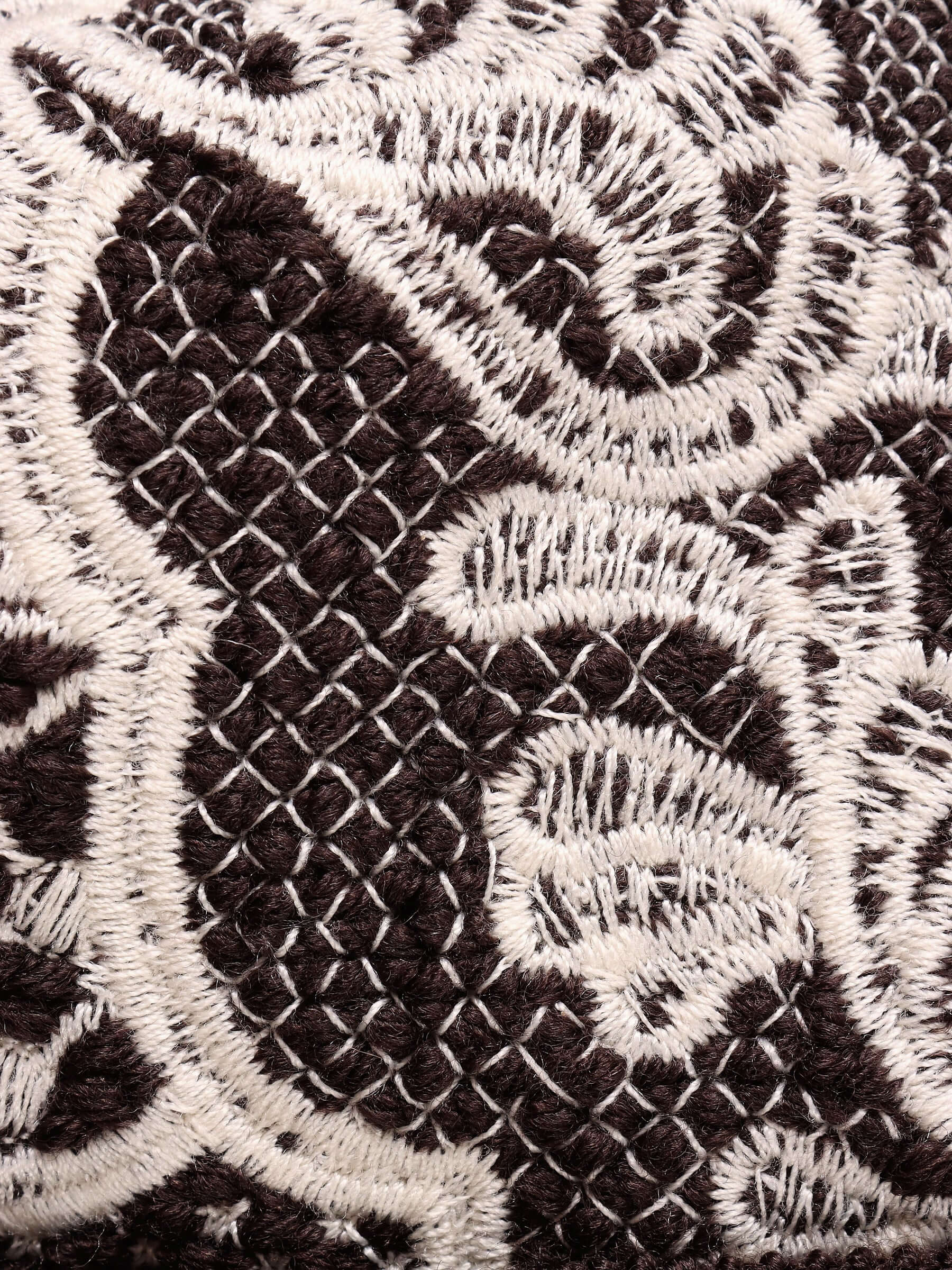 A very close-up shot of the intricate white lace-like floral embroidery on the dark brown wool. 