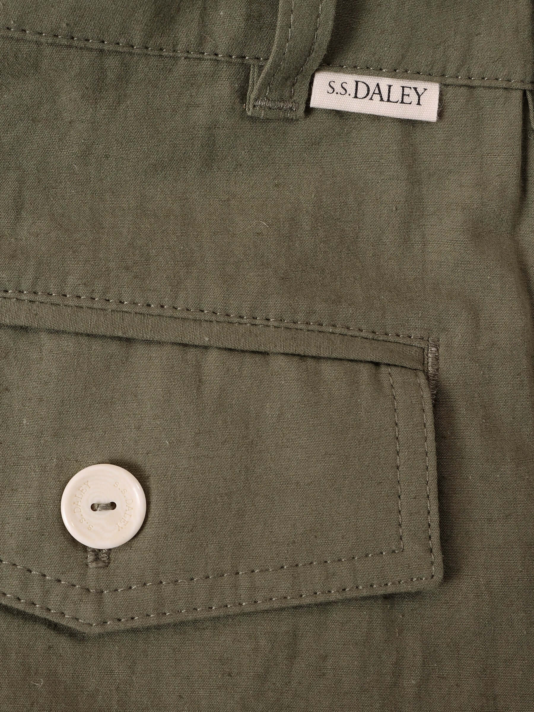 A close-up of the 'Clarence' Trouser's khaki green Japanese cotton-blend material, Back pocket with a white S.S.DALEY engraved button and small S.S.DALEY tag by the belt loop.