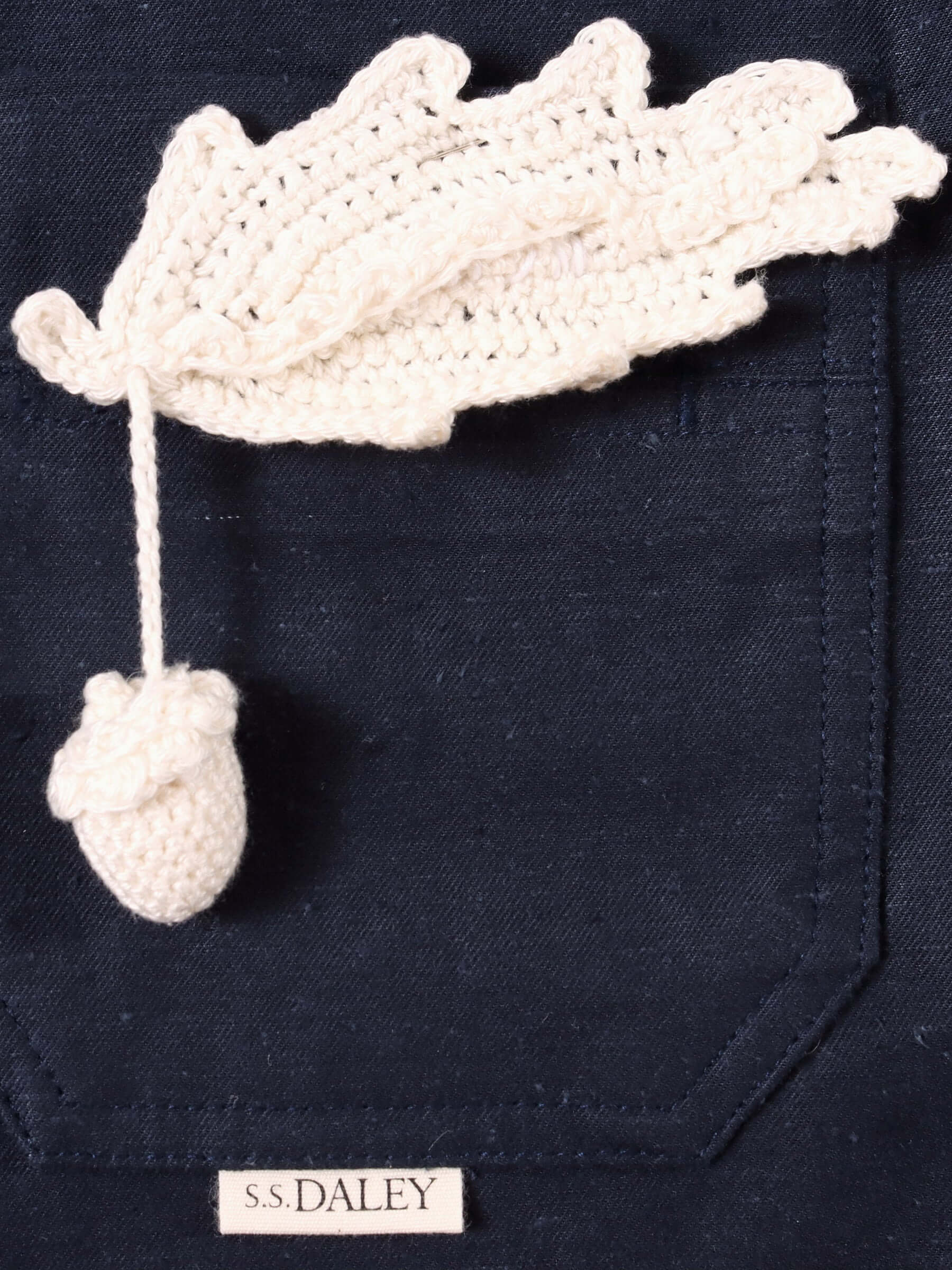 A close up of the hand-crocheted acorn pin and the top front pocket, as well as a small S.S.DALEY logo just under the pocket.