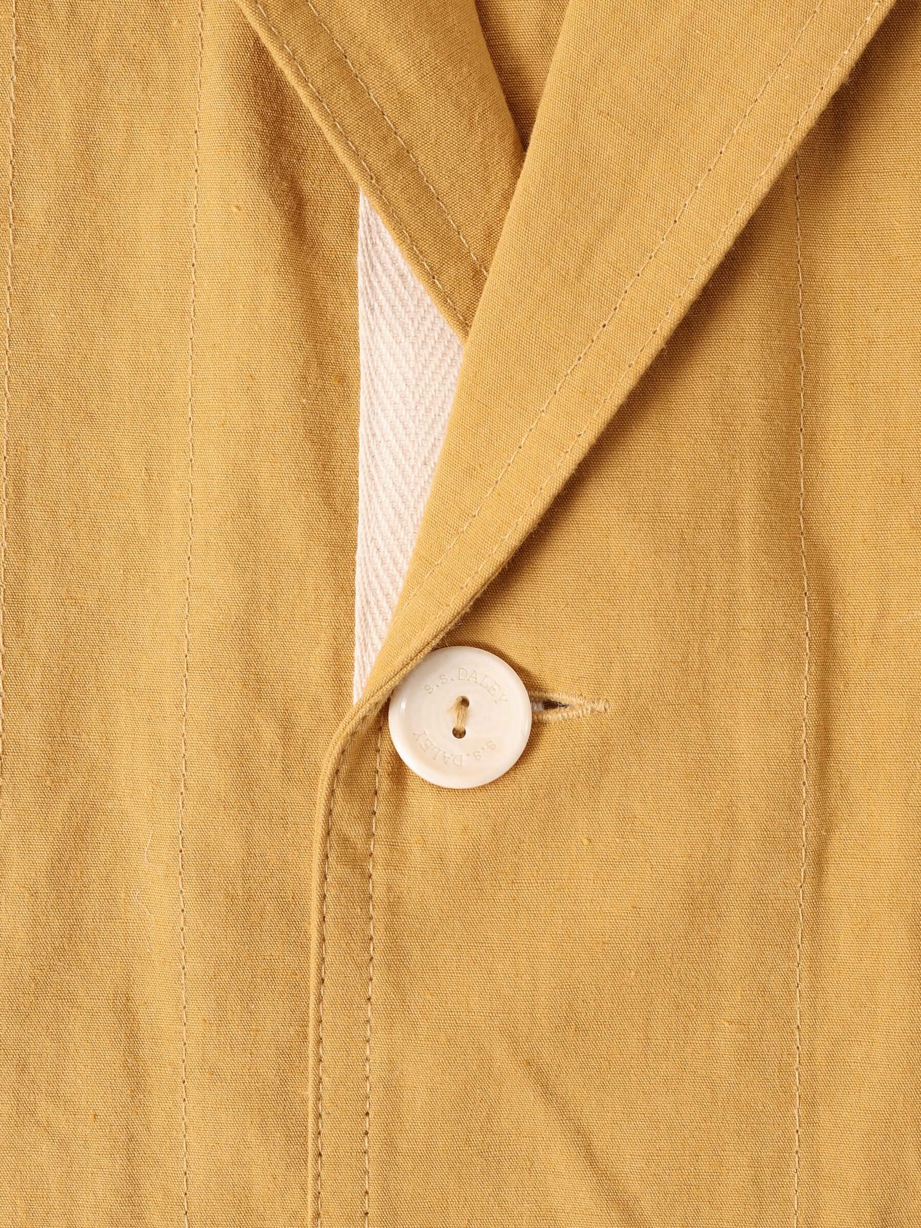 A close-up of the 'Clarence' Chore Jacket in mustard's button hole and ecru S.S.Daley engraved button.