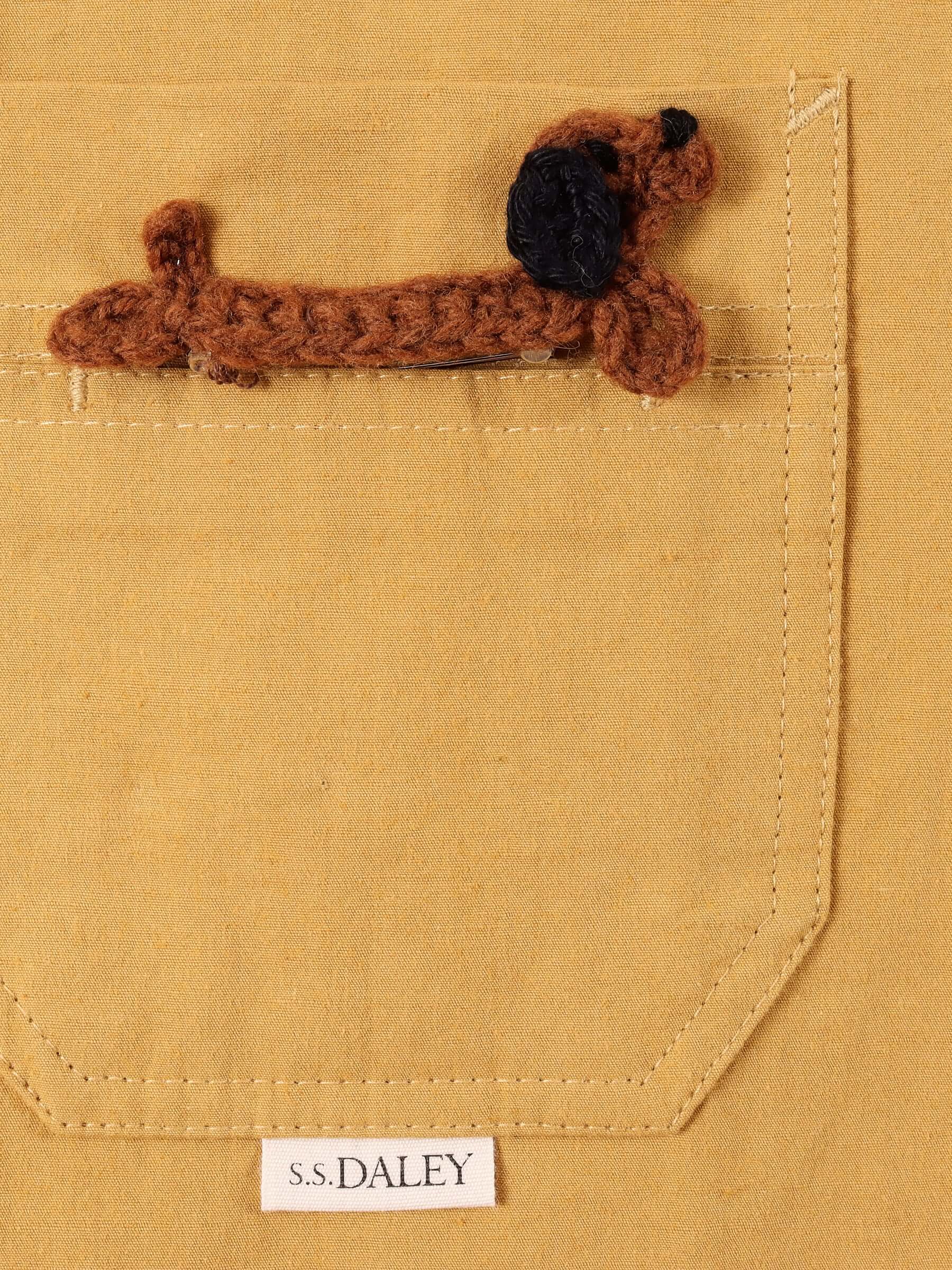 A close-up of the chest pocket with the detachable crocheted Dachshund pin and a small S.S.DALEY logo underneath the pocket of the mustard 'Clarence' Chore Jacket.