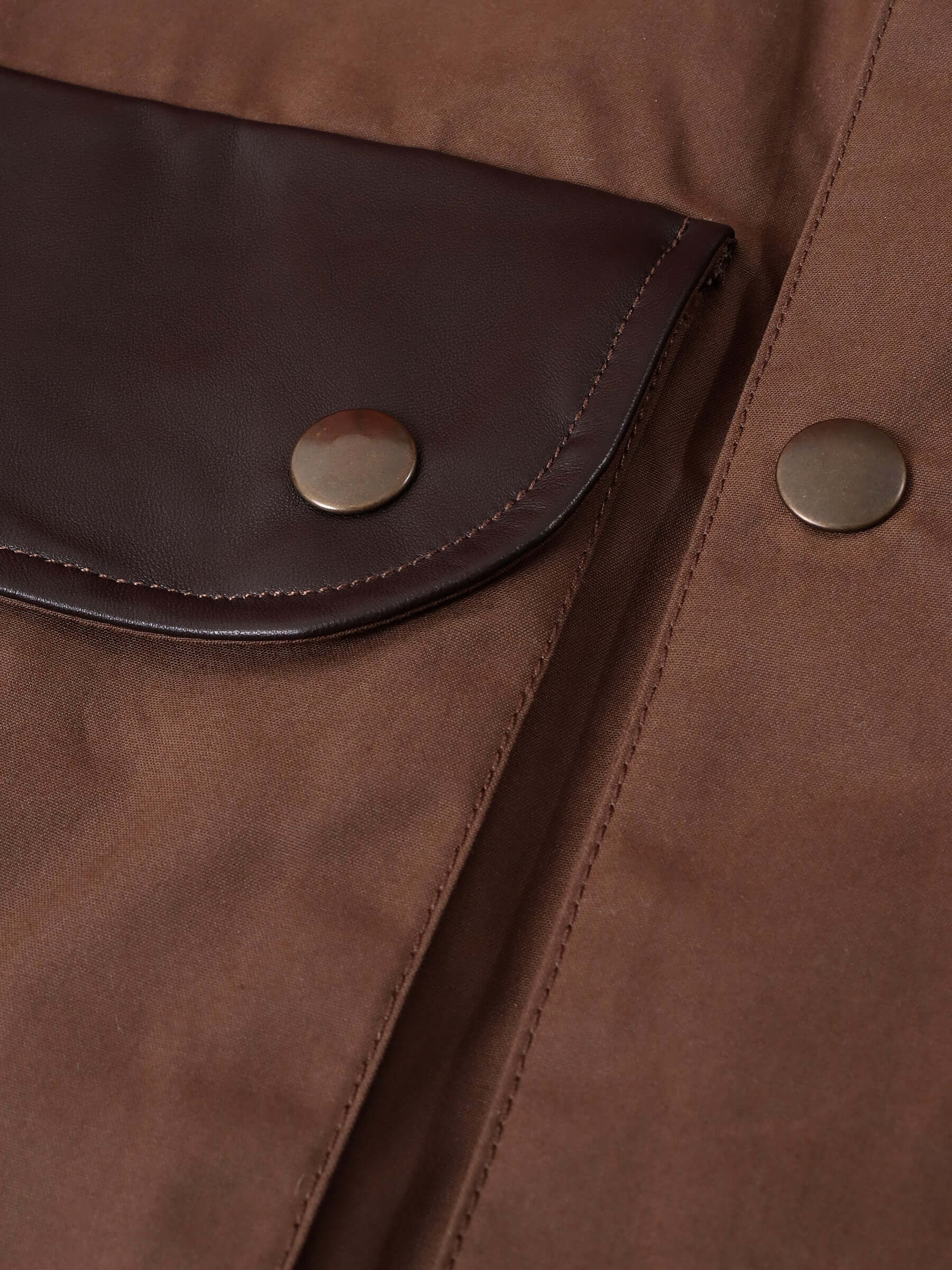 A detail shot of the British milled cotton with water resistant waxed coating and Nappa leather pocket details with circular brass snap buttons.